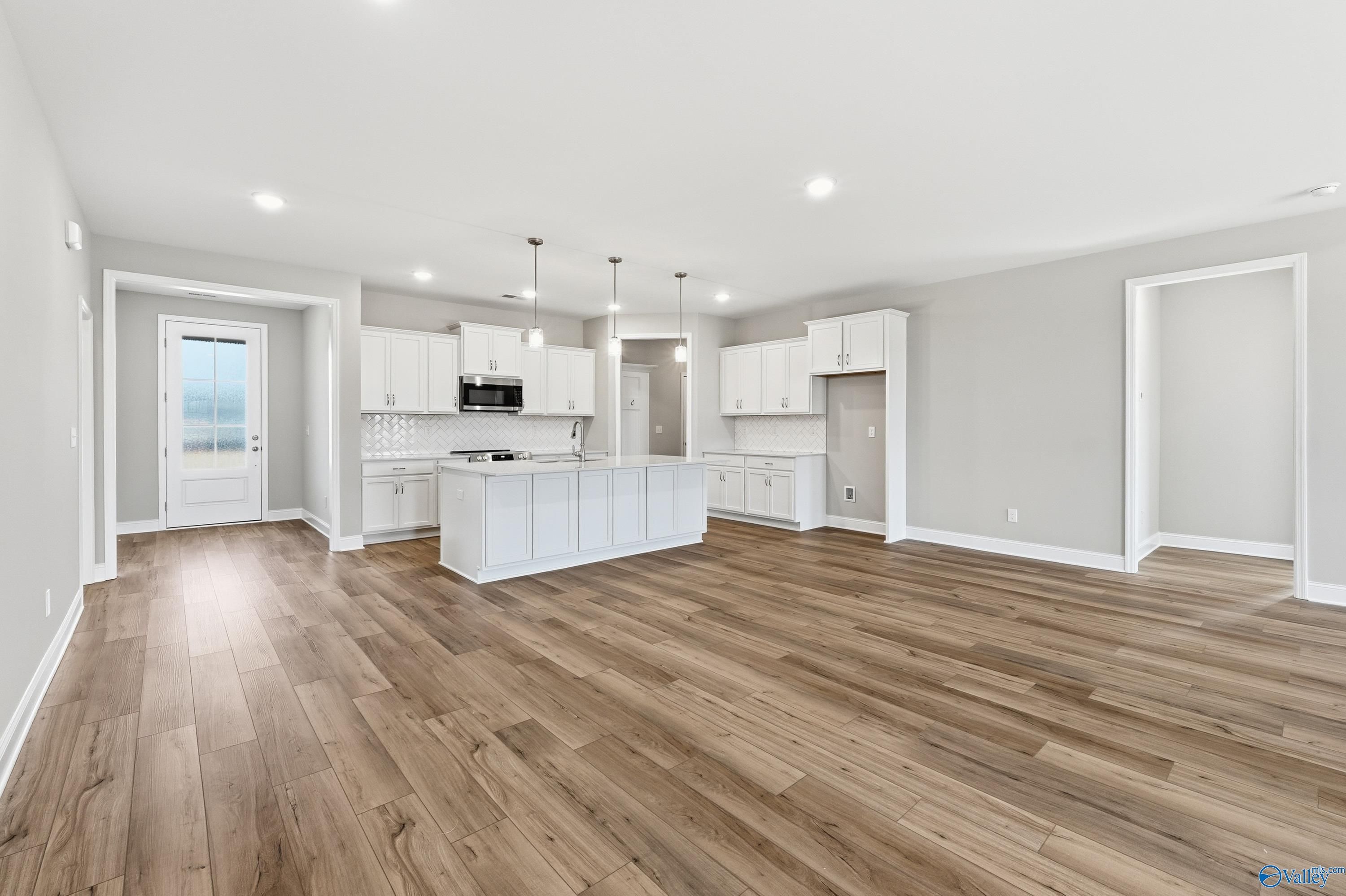 Modern open-concept kitchen with white cabinets, large island, stainless appliances, and hardwood floors in The Lanier home, Meridianville, Alabama