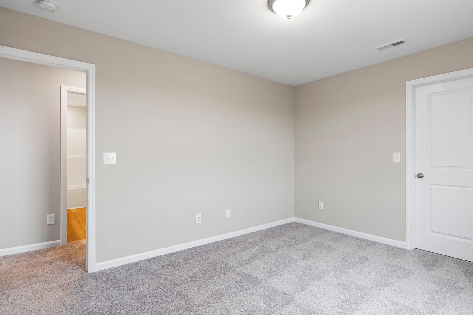 Spacious secondary bedroom in The Stella A with beige walls, gray carpet, ensuite bath door, and closet entry