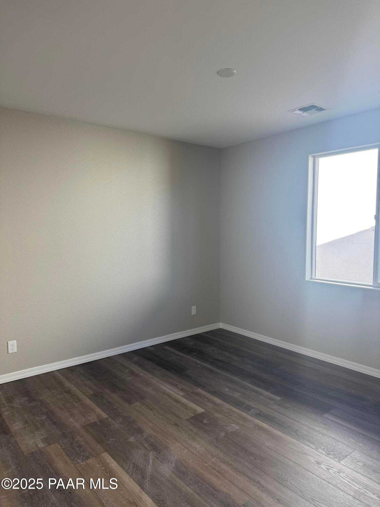 Spacious bedroom with beige walls, hardwood floors, and large window in Davidson Homes The Monarch E, Prescott, Arizona