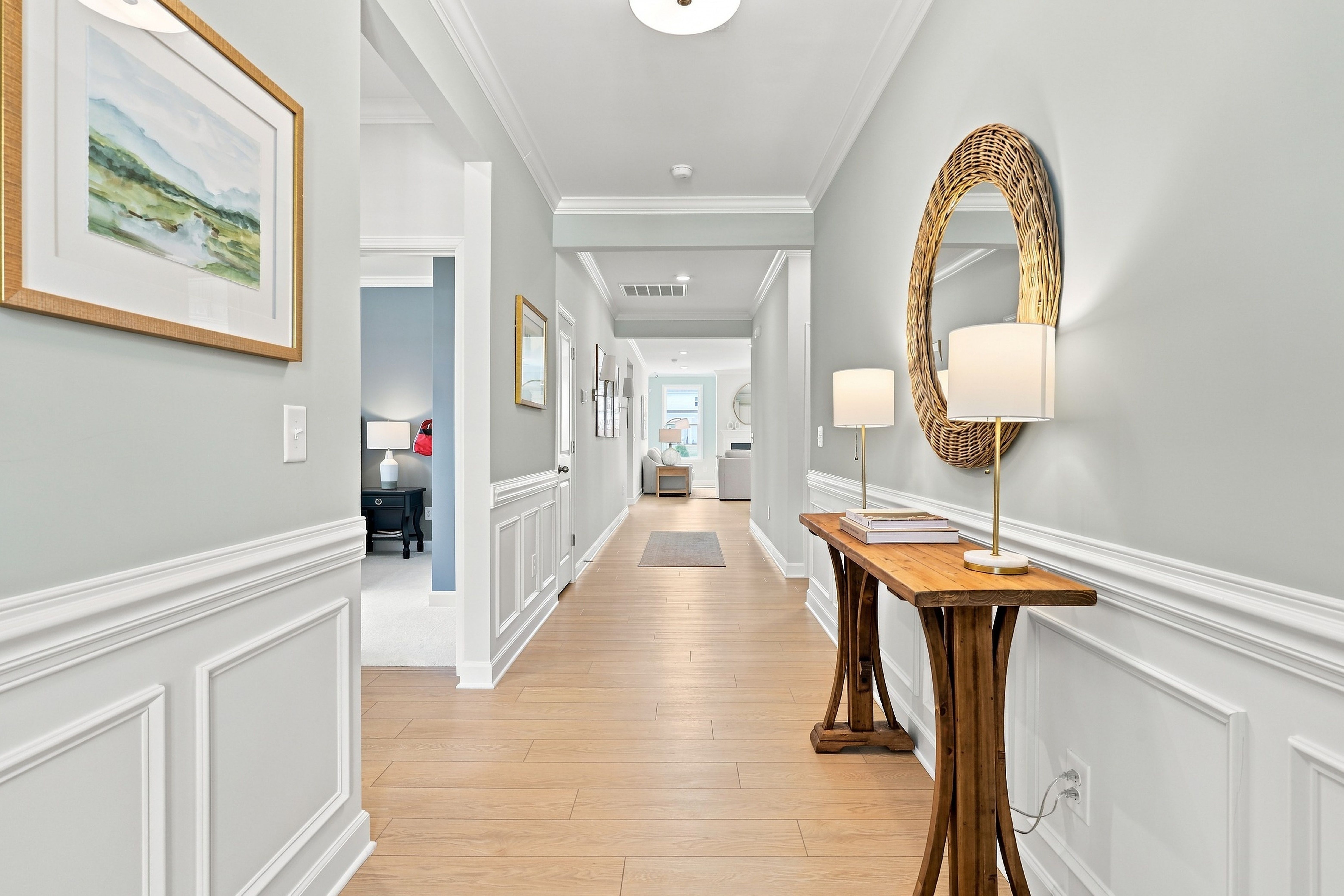Bright, open foyer hallway in The Daphne D featuring wood flooring, wainscoting, and a stylish console table with a mirror.