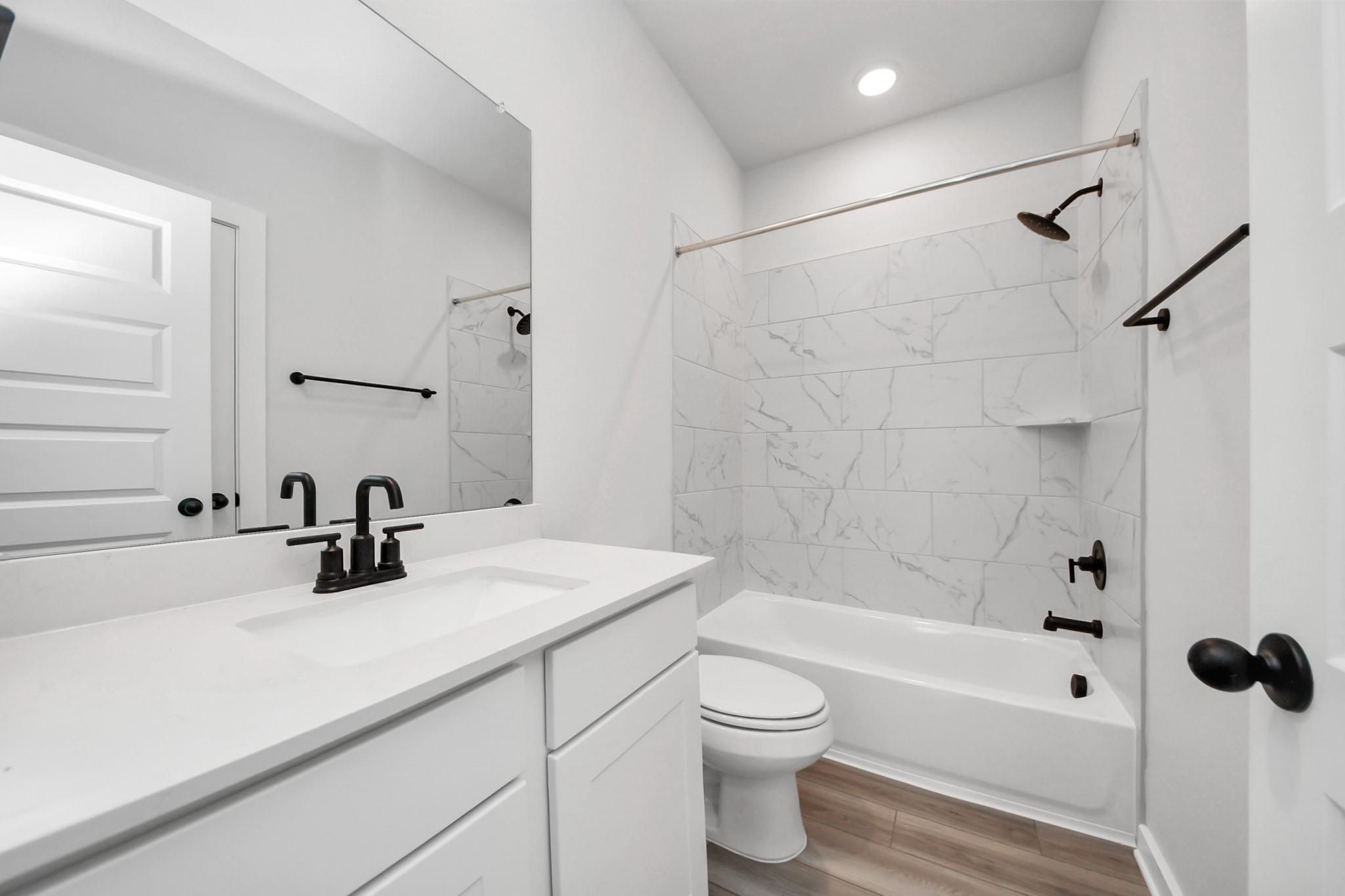 Modern bathroom with white vanity, marble-look tile tub surround, and matte black fixtures in The Everett C, Dayton, Texas.