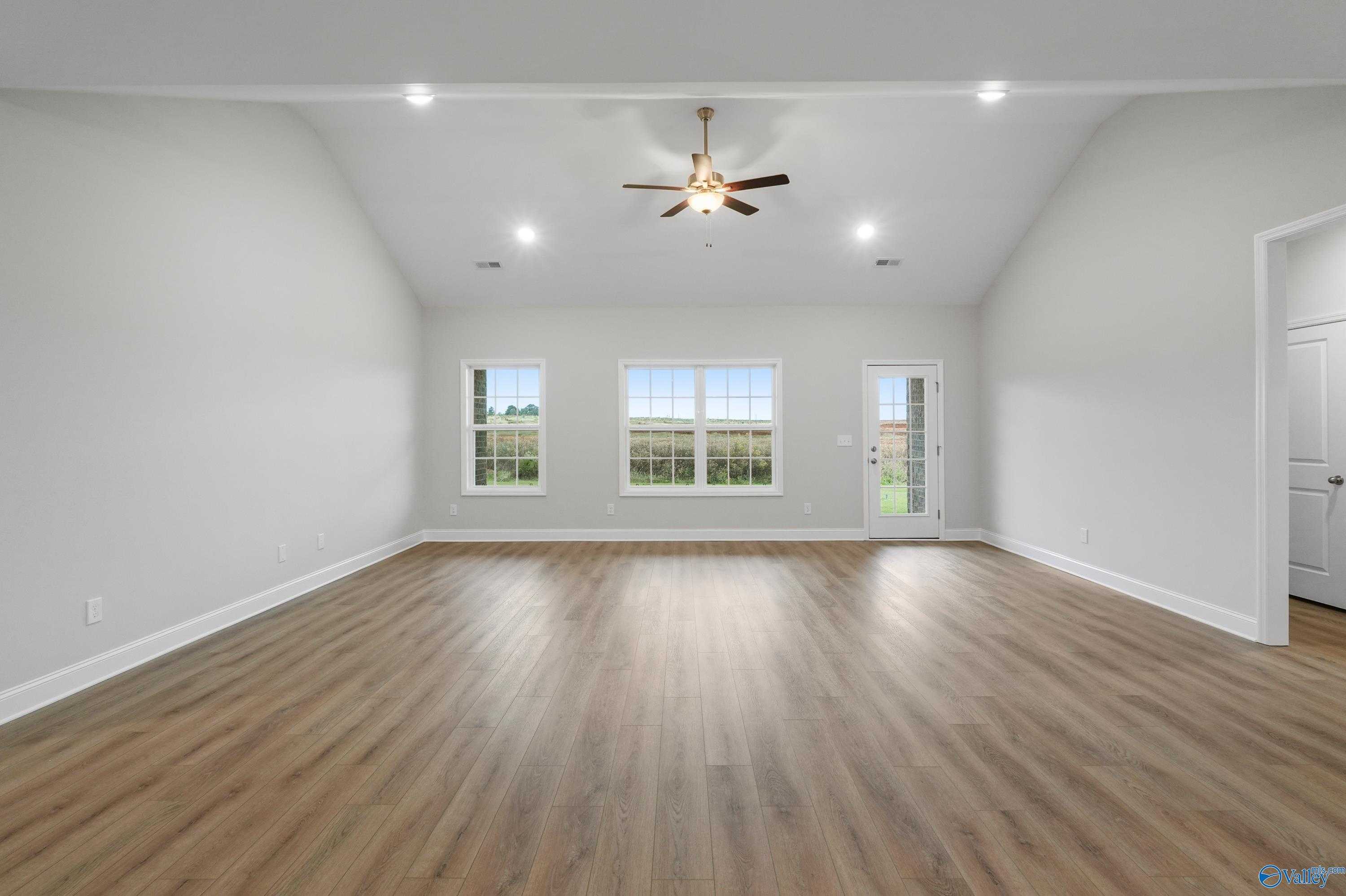 Spacious living room with vaulted ceiling, ceiling fan, large windows, and hardwood floors in Davidson Homes The Lanier, Harvest, Alabama