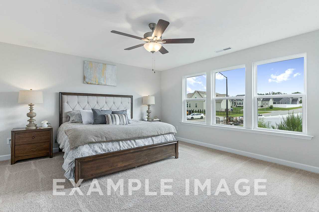 Spacious master bedroom in The Willow C featuring king bed with tufted headboard, ceiling fan, and scenic pond views through triple windows