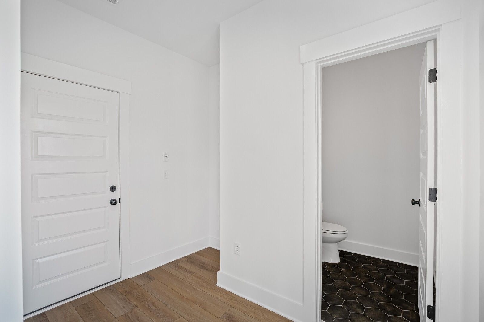 Elegant powder room with white toilet, black hexagonal tile floor, and white walls in Davidson Homes The Willow C, Gallatin, TN