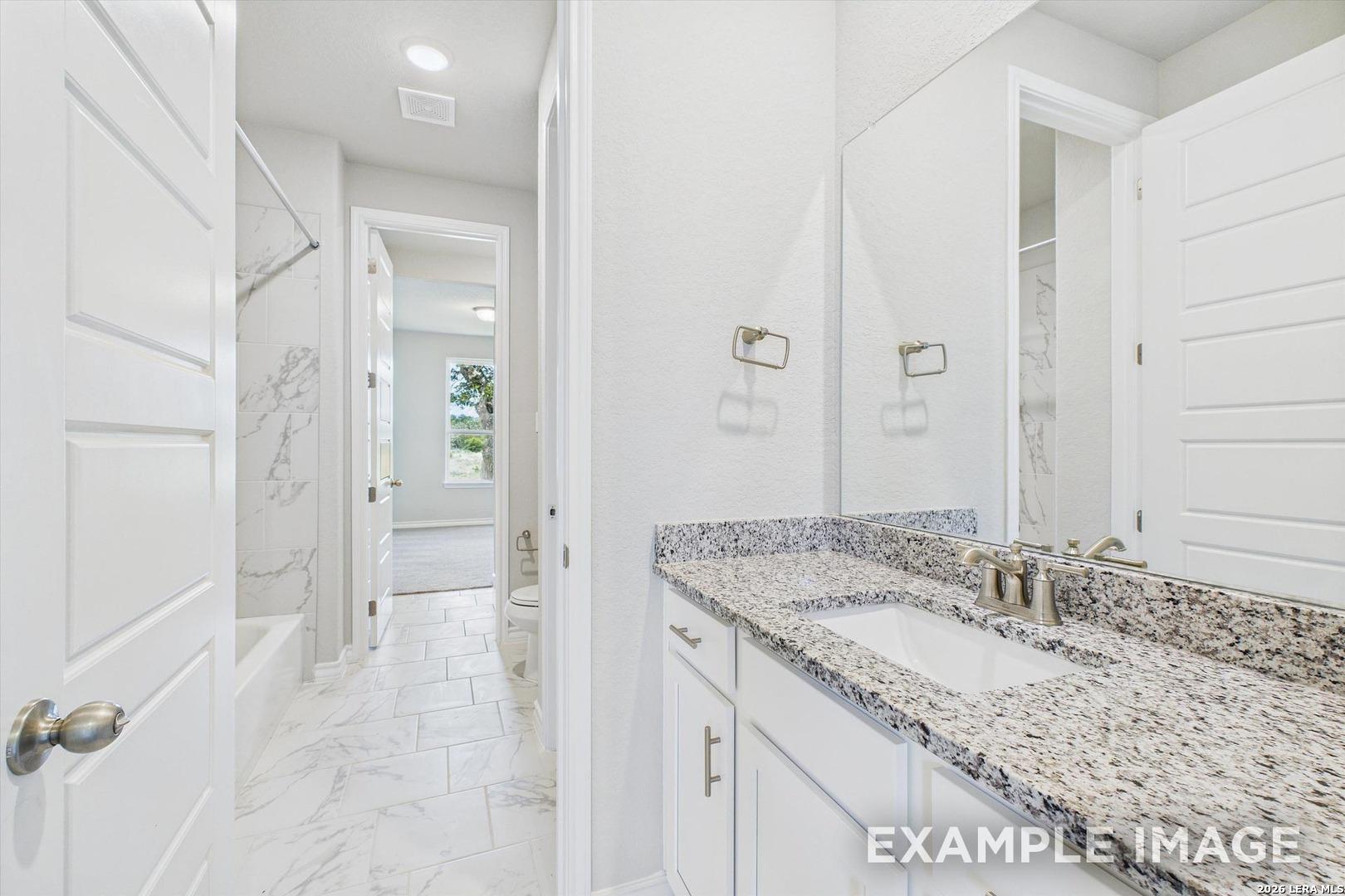 Modern bathroom with granite vanity, marble-look tile, and tub shower in The Foster F floor plan, Potranco Oaks, Castroville.