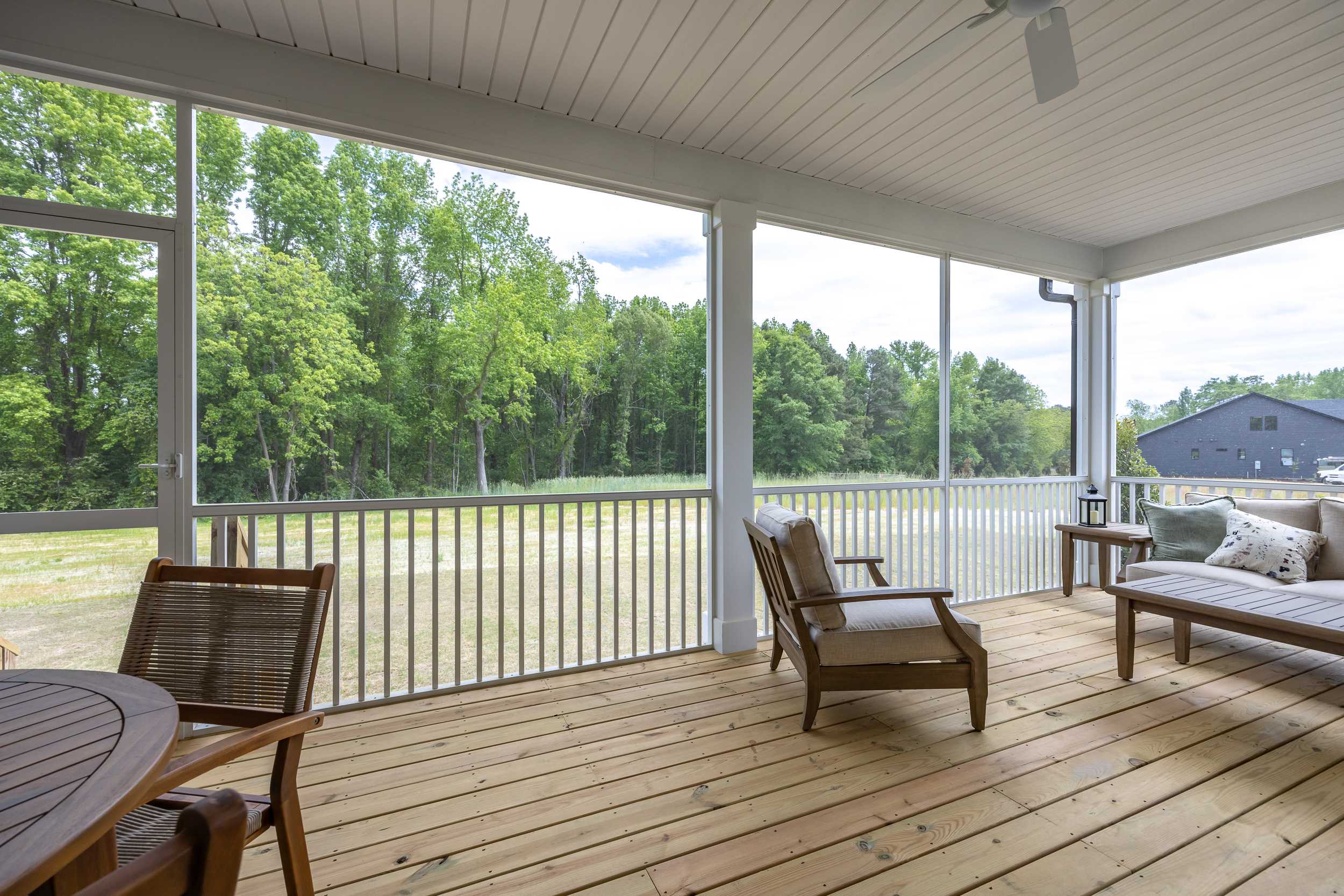 Spacious screened porch in The Magnolia A with wicker chairs, ceiling fan, and lush woodland view