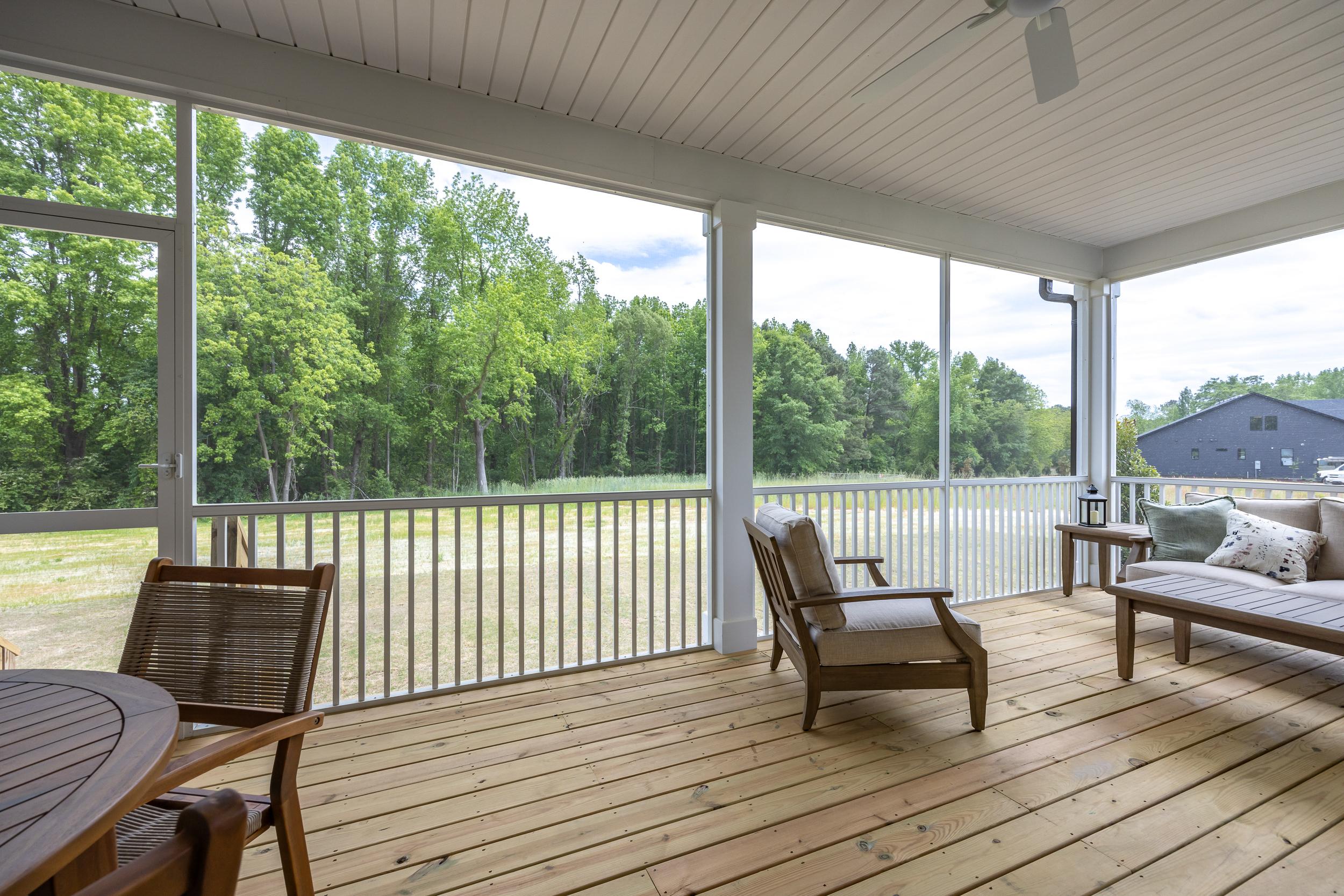 Spacious screened porch of The Magnolia A with wooden deck, lounge chairs, and tree-lined view in Holly Springs NC
