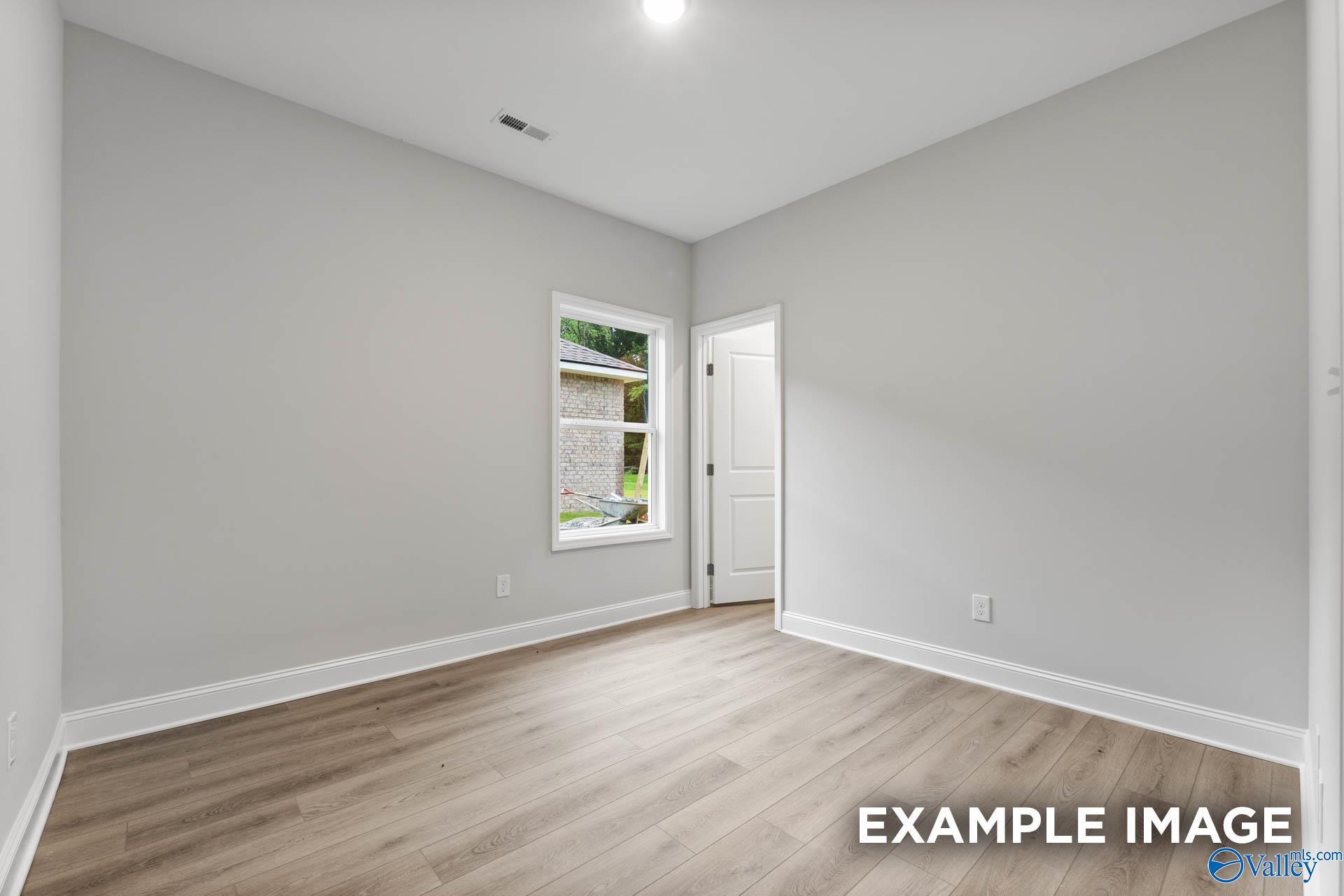 Spacious secondary bedroom with neutral gray walls, large window, and light wood floors in Davidson Homes The Daphne, Meridianville AL