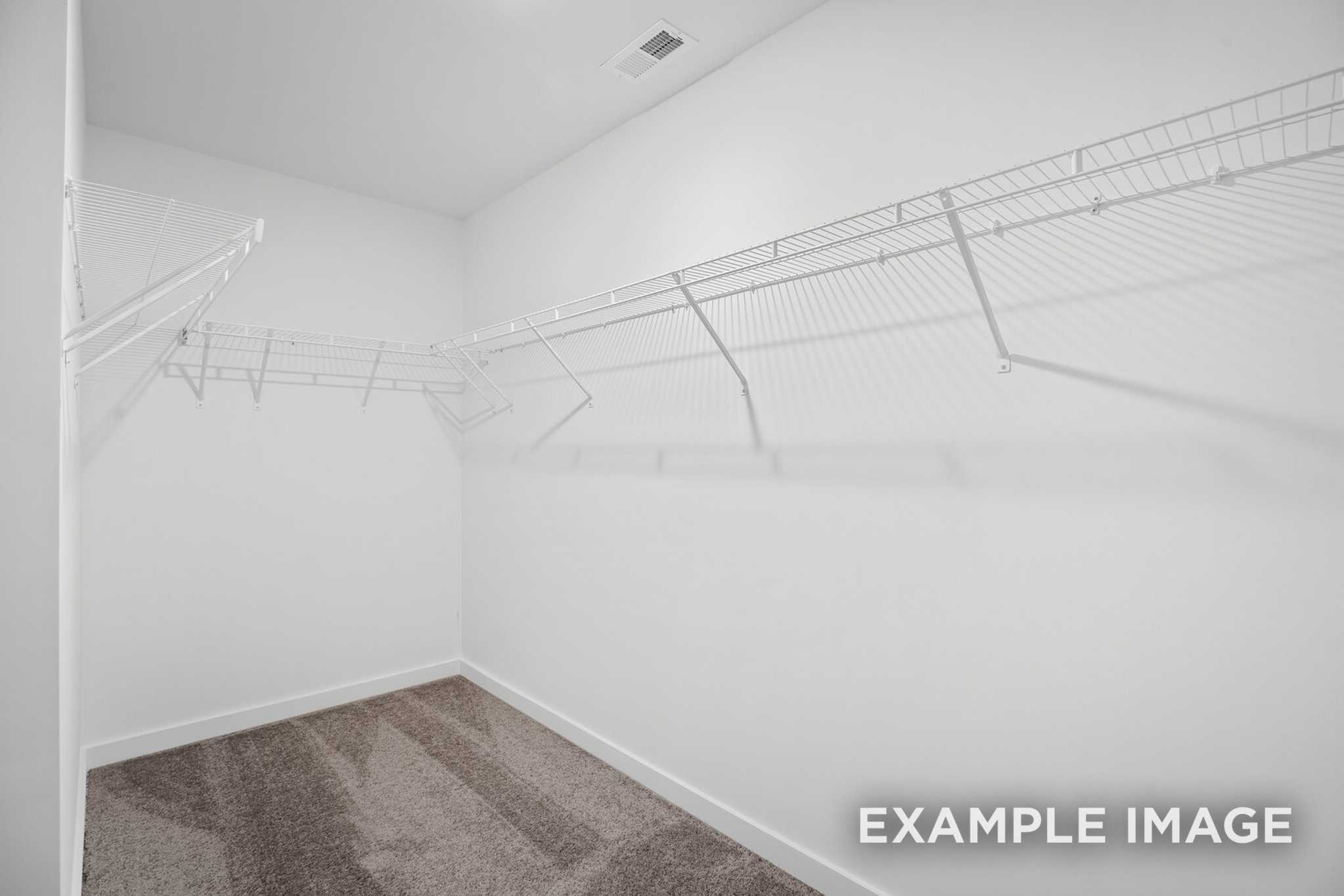Spacious walk-in closet in The Grayson C master suite with white wire shelving and beige carpet floor