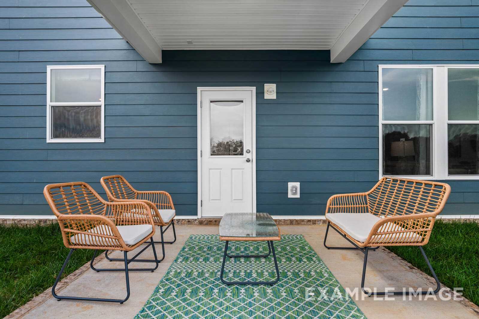 The Gordon B covered patio featuring wicker armchairs, glass-top table, and teal rug against blue siding home exterior