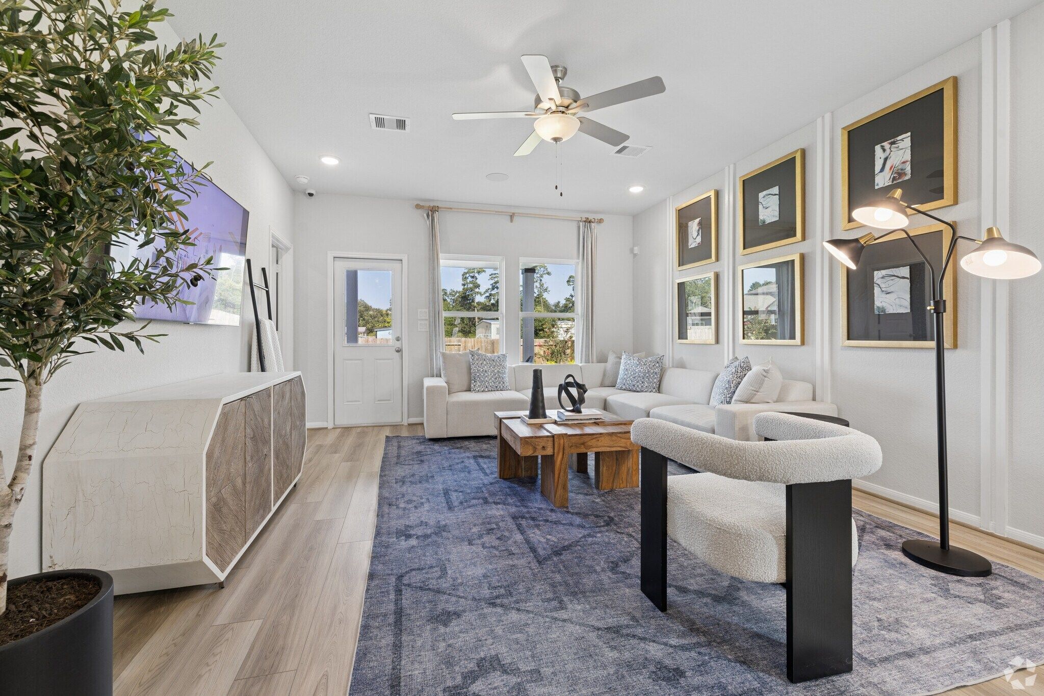Spacious living room at Liberty Estates in Cleveland Texas with L-shaped sofa, hardwood floors, ceiling fan, wall art, and TV