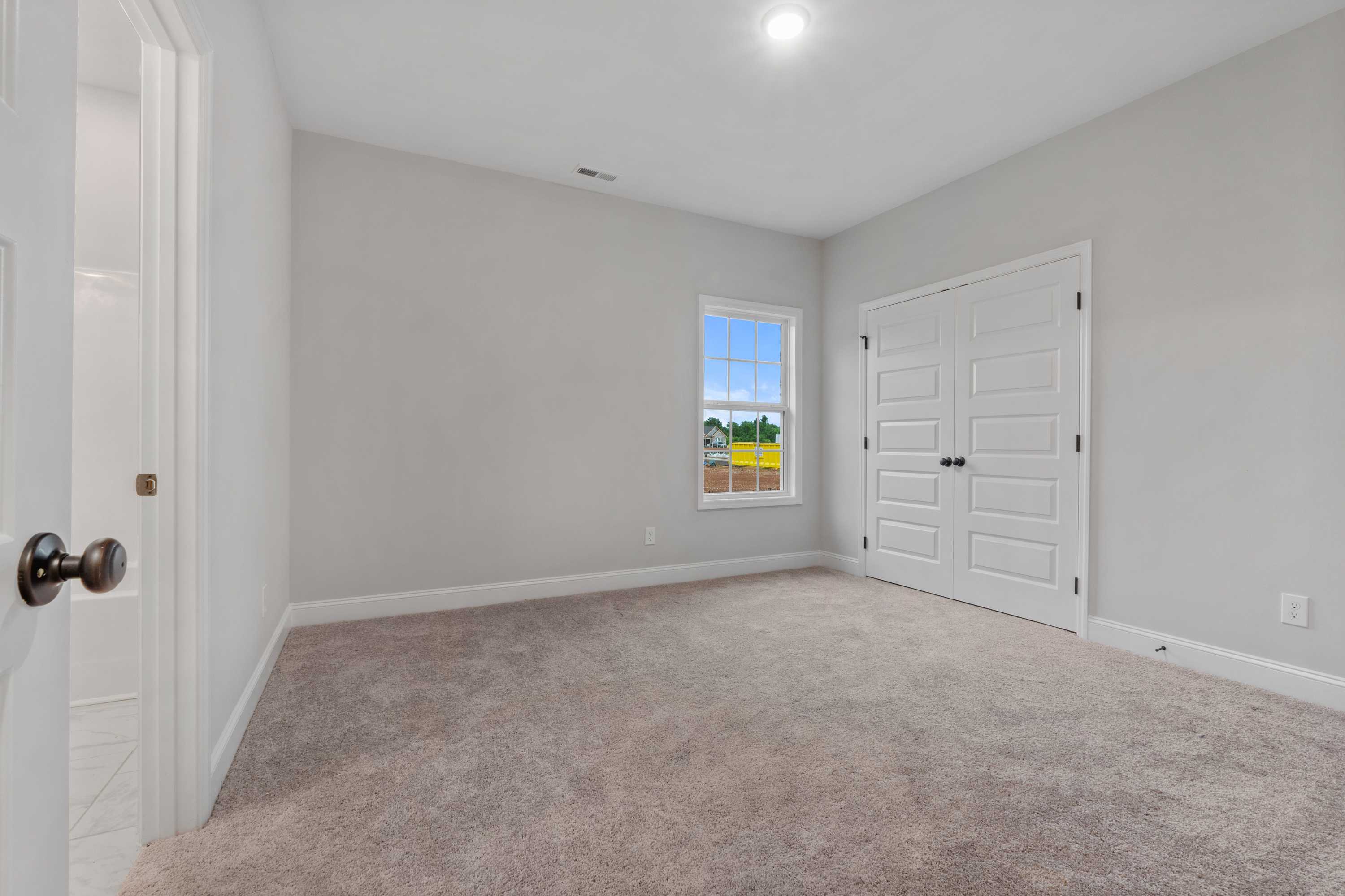 Spacious secondary bedroom in The Oxford home design with gray walls, carpet flooring, double closet doors, and window overlooking fields