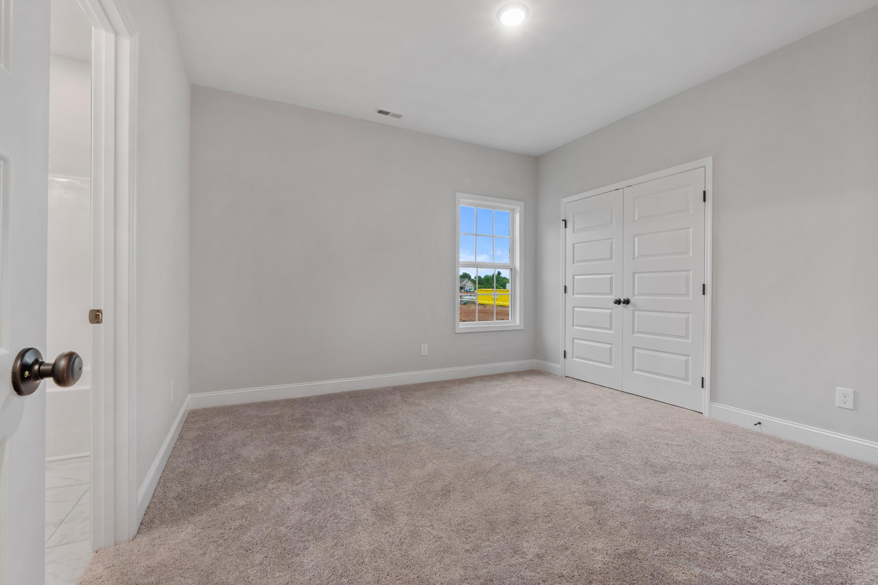 Spacious secondary bedroom in The Oxford home design with gray walls, carpet flooring, double closet doors, and window overlooking fields