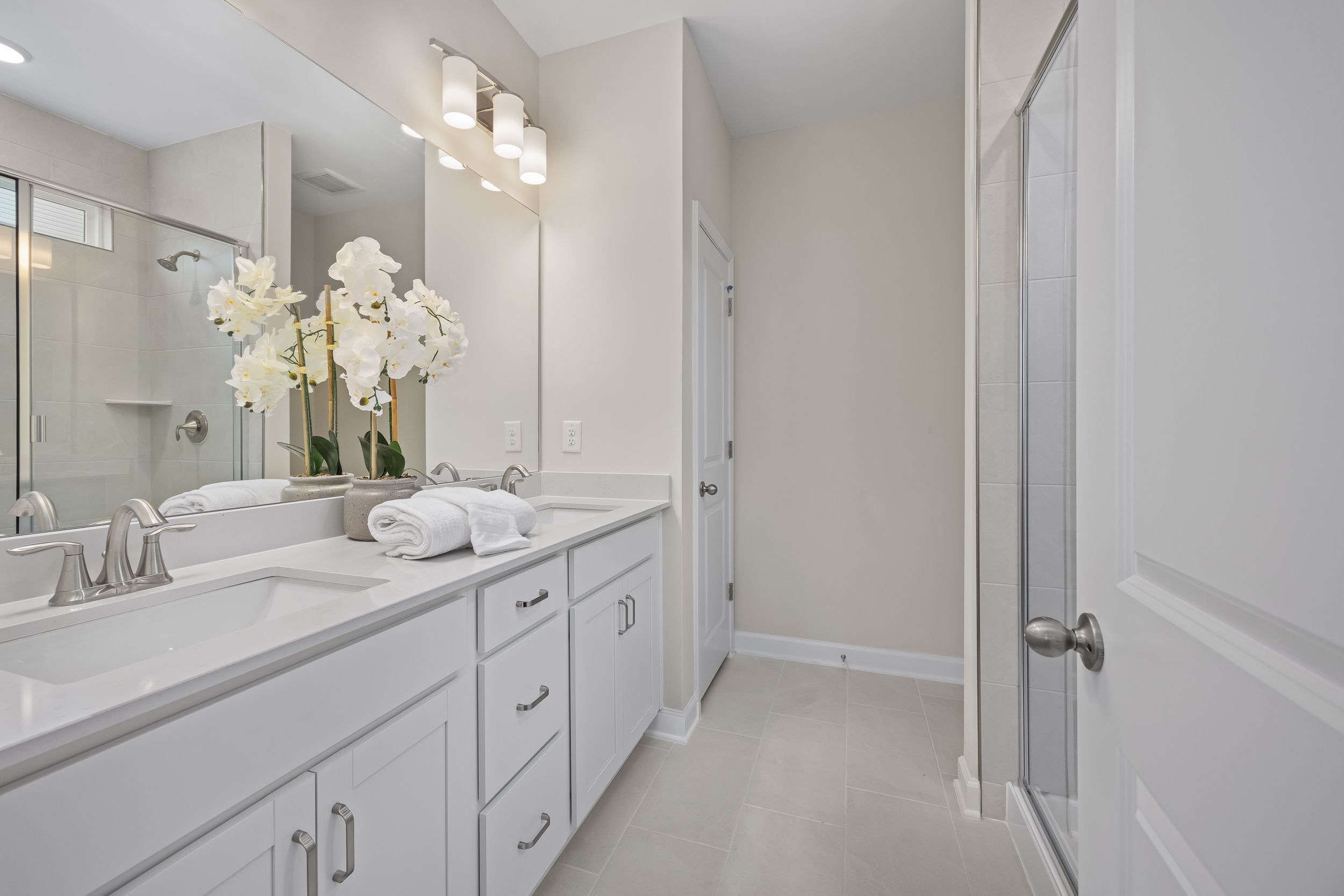 Modern primary bathroom at Gregory Village in Lillington, NC, featuring a dual vanity with white cabinets and a glass shower.
