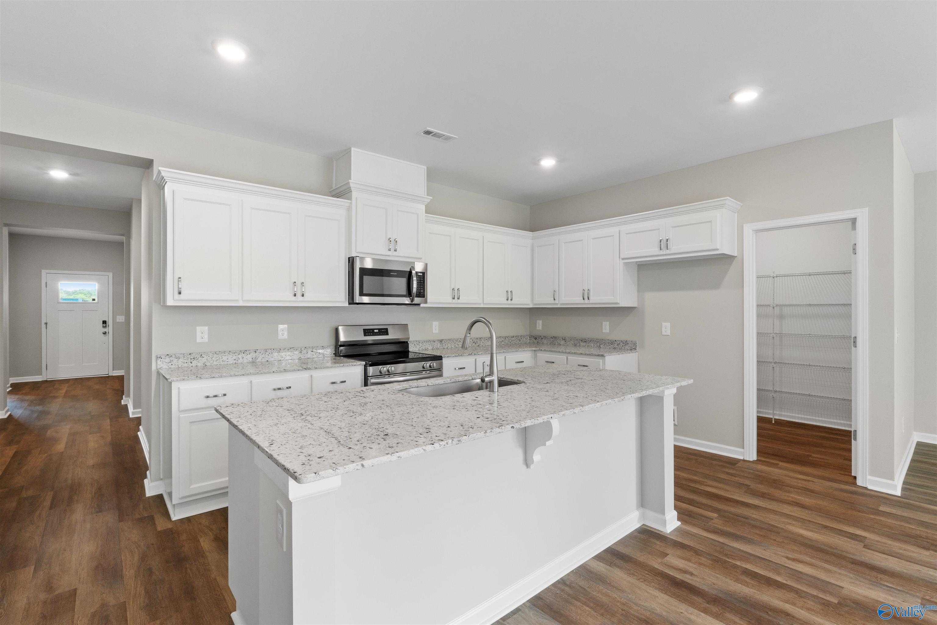 Modern white kitchen with granite countertops, stainless steel appliances, and large island in Davidson Homes The Luna, Hazel Green, Alabama