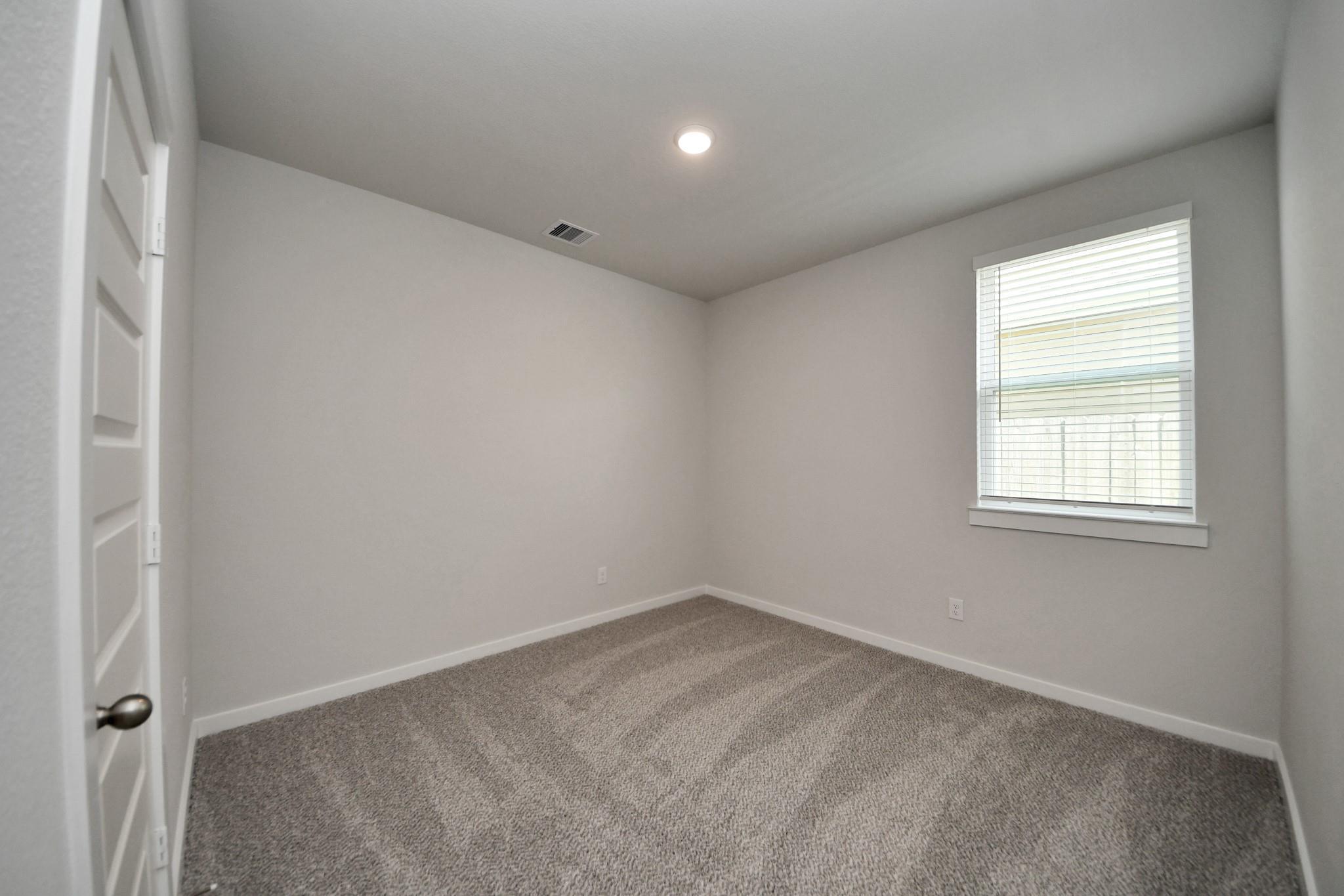 Bright empty bedroom with carpet flooring, white walls, and window with blinds in Davidson Homes The Frio F, Robins Landing Houston