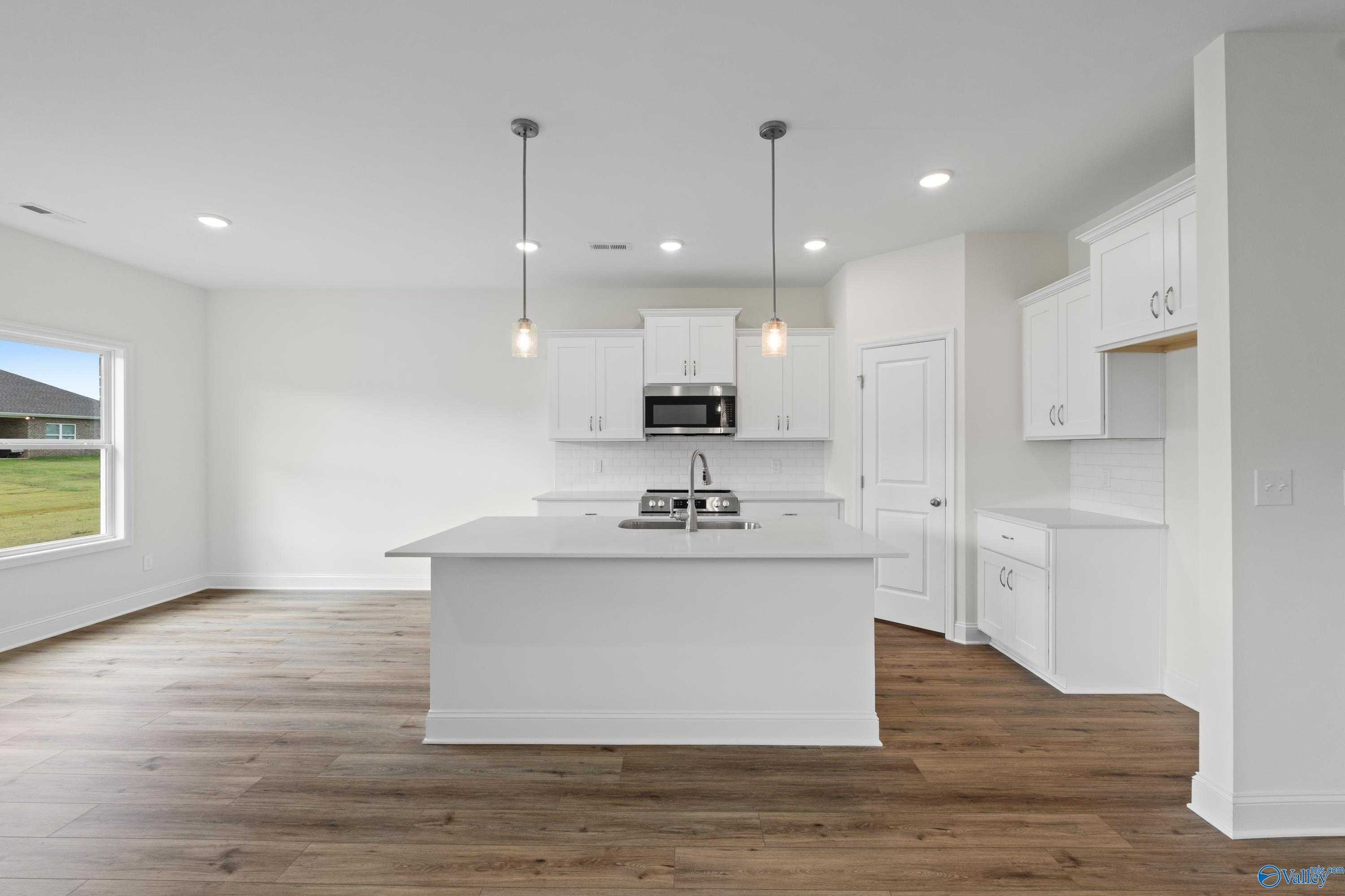 Spacious white kitchen with large island, stainless appliances, pendant lights in The Asheville C by Davidson Homes, Athens, AL