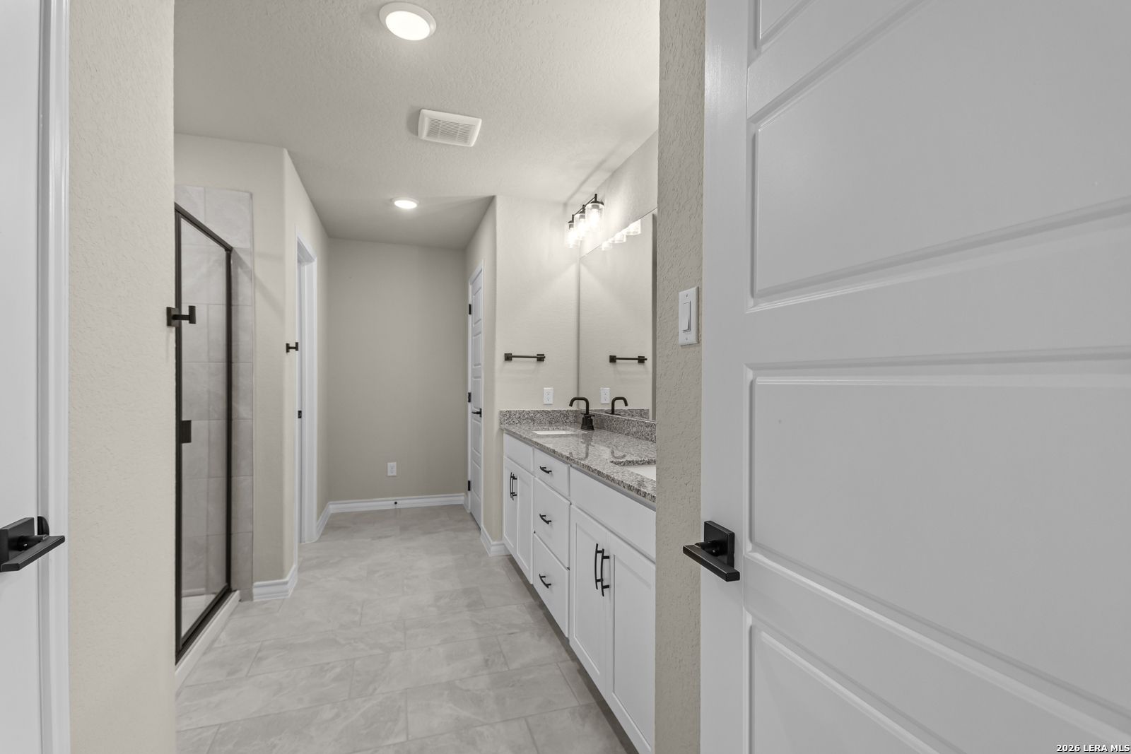 Modern bathroom with dual vanity, granite countertops, and walk-in shower in The Danbury H, The Reserve at Potranco Oaks.
