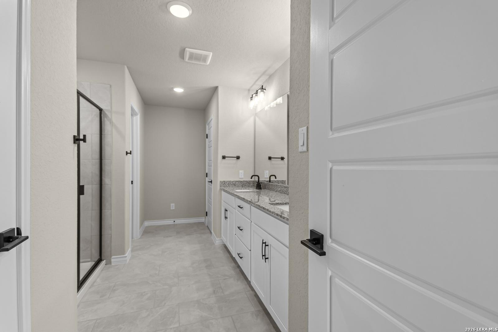 Modern bathroom with dual vanity, granite countertops, and walk-in shower in The Danbury H, The Reserve at Potranco Oaks.