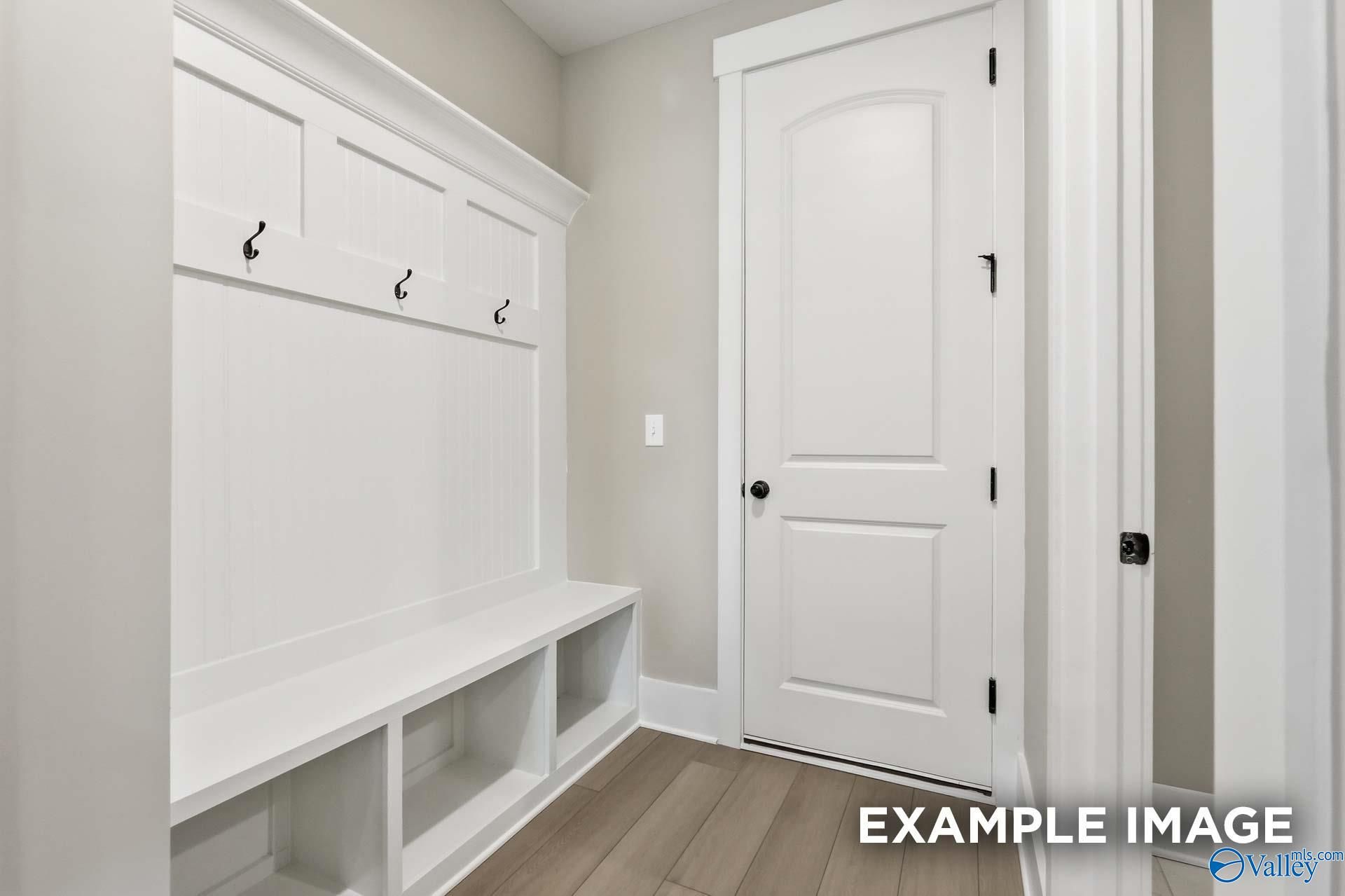 Built-in white mudroom bench and coat hooks with open storage shelves in Davidson Homes The Emory, Decatur, Alabama