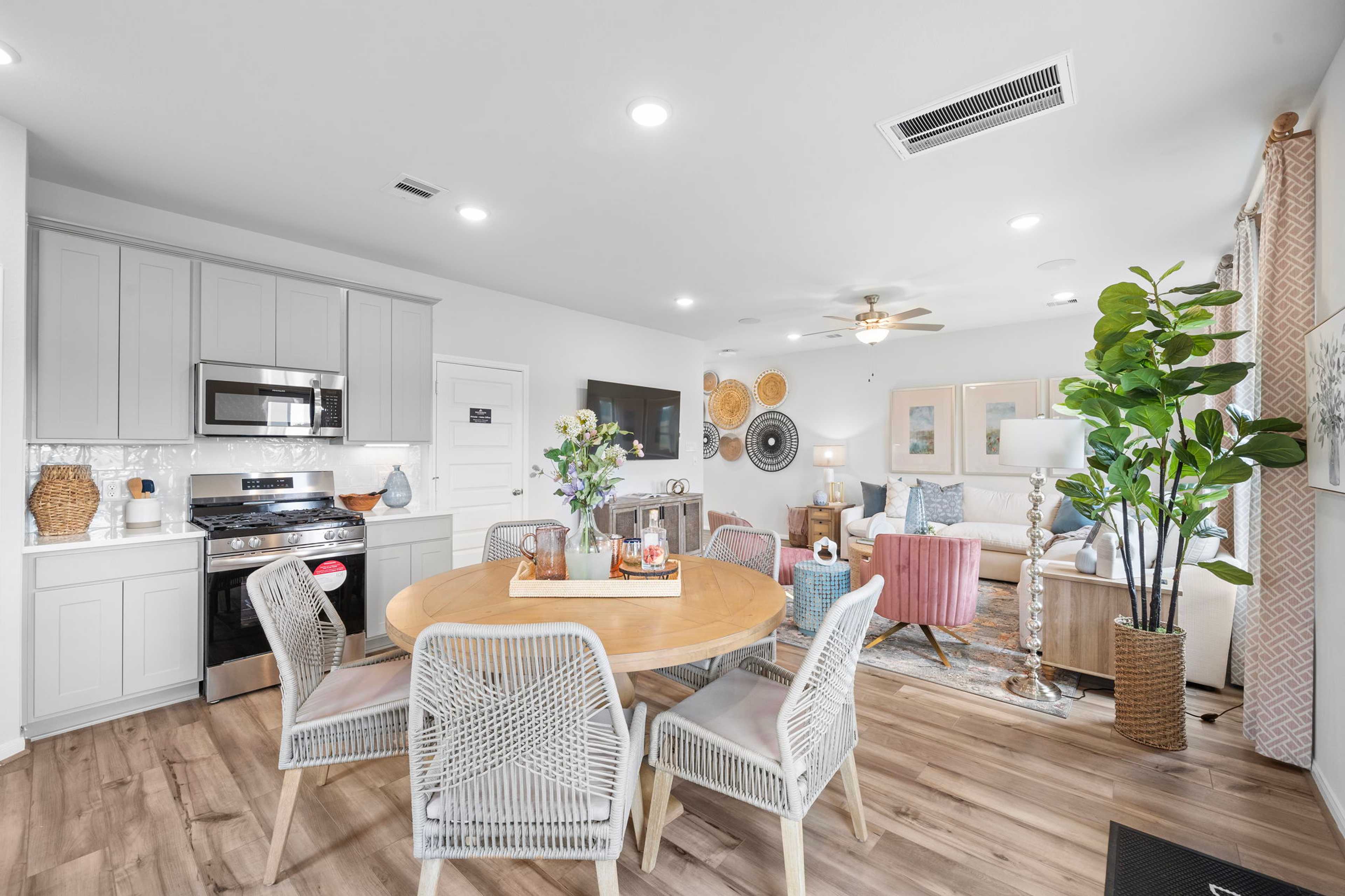 Open-concept kitchen dining area at Spring Branch Crossing in Conroe TX with gray cabinets, round wooden table, rattan chairs, and hardwood floors
