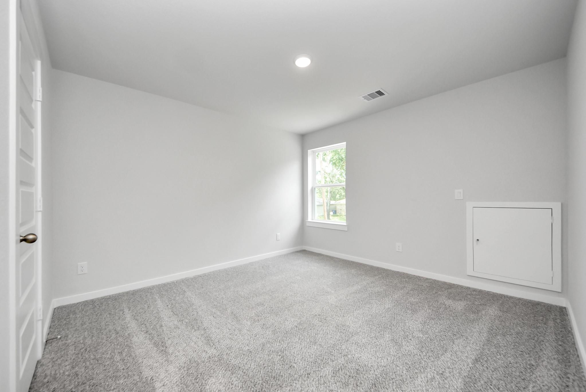 Bright, carpeted bedroom with attic access in The Sabine E floor plan at Windmill Estates in Magnolia, Texas.