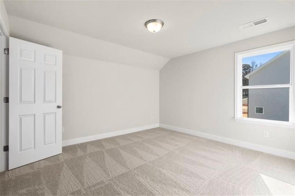 Bright, carpeted bedroom with neutral walls in The Ash C floor plan at Wehunt Meadows in Hoschton, Georgia.