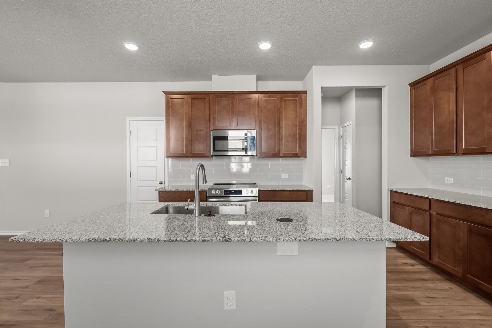 Modern kitchen with granite island, wood cabinets, and stainless appliances in The Frio G floor plan at Heartland, Texas.
