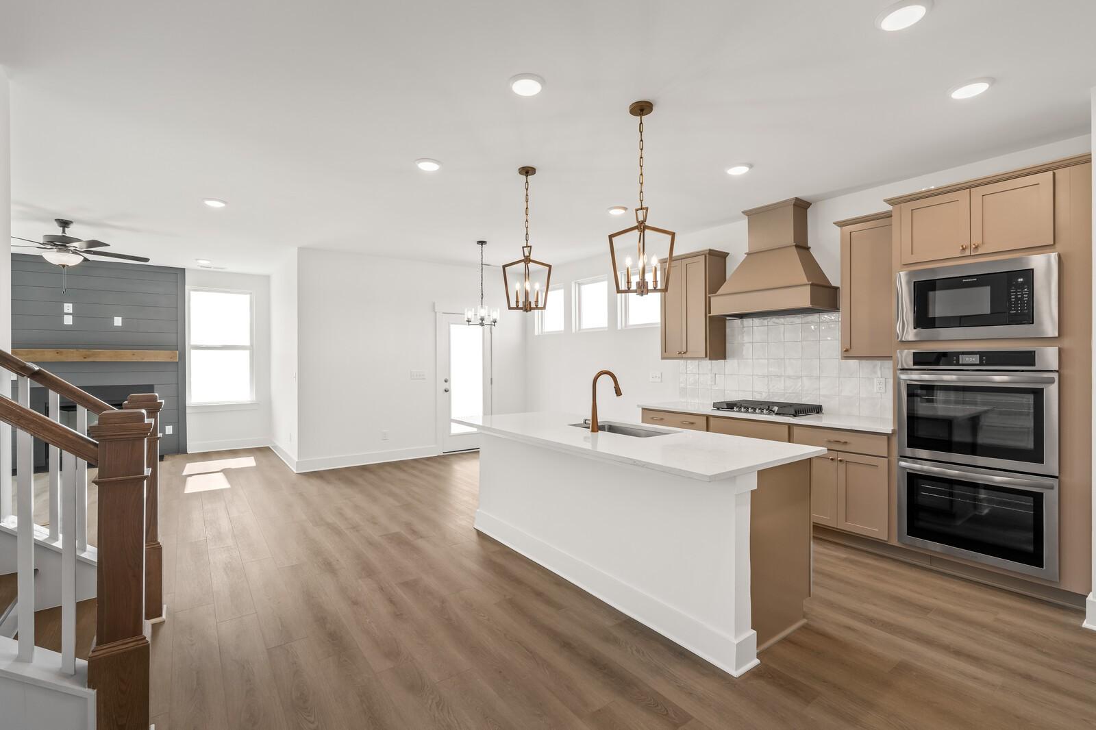 Open-concept kitchen with white island, stainless double ovens, beige cabinets, and hardwood floors in The Ash A, Gallatin, TN