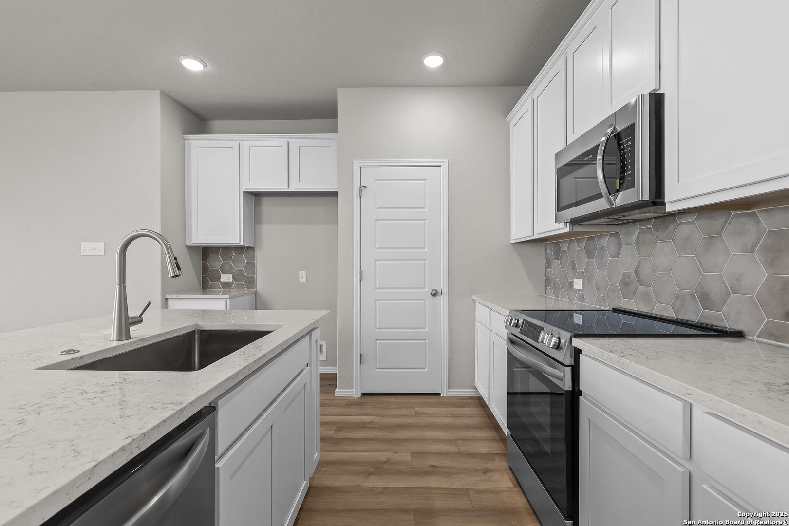 Modern kitchen with white cabinets, quartz island, stainless appliances, hex tile backsplash in Davidson Homes Colorado B, San Antonio