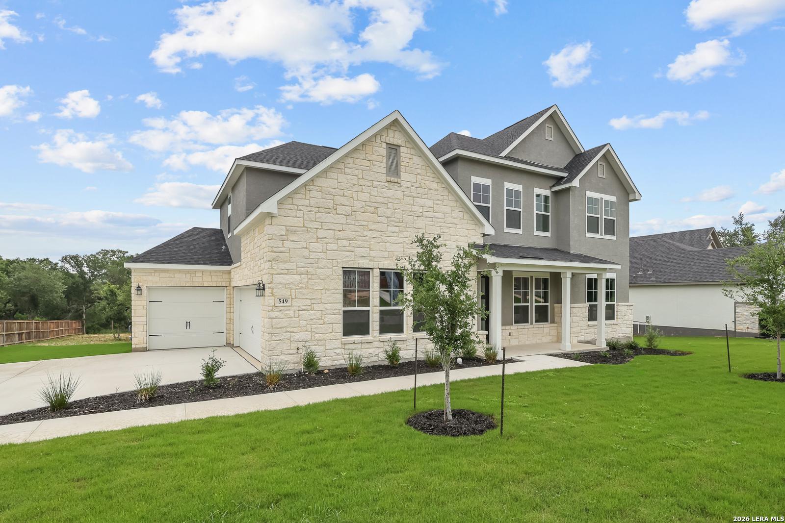 Modern two-story stone and siding home with front porch, 3-car garage, landscaped yard in Potranco Oaks, Castroville, Texas