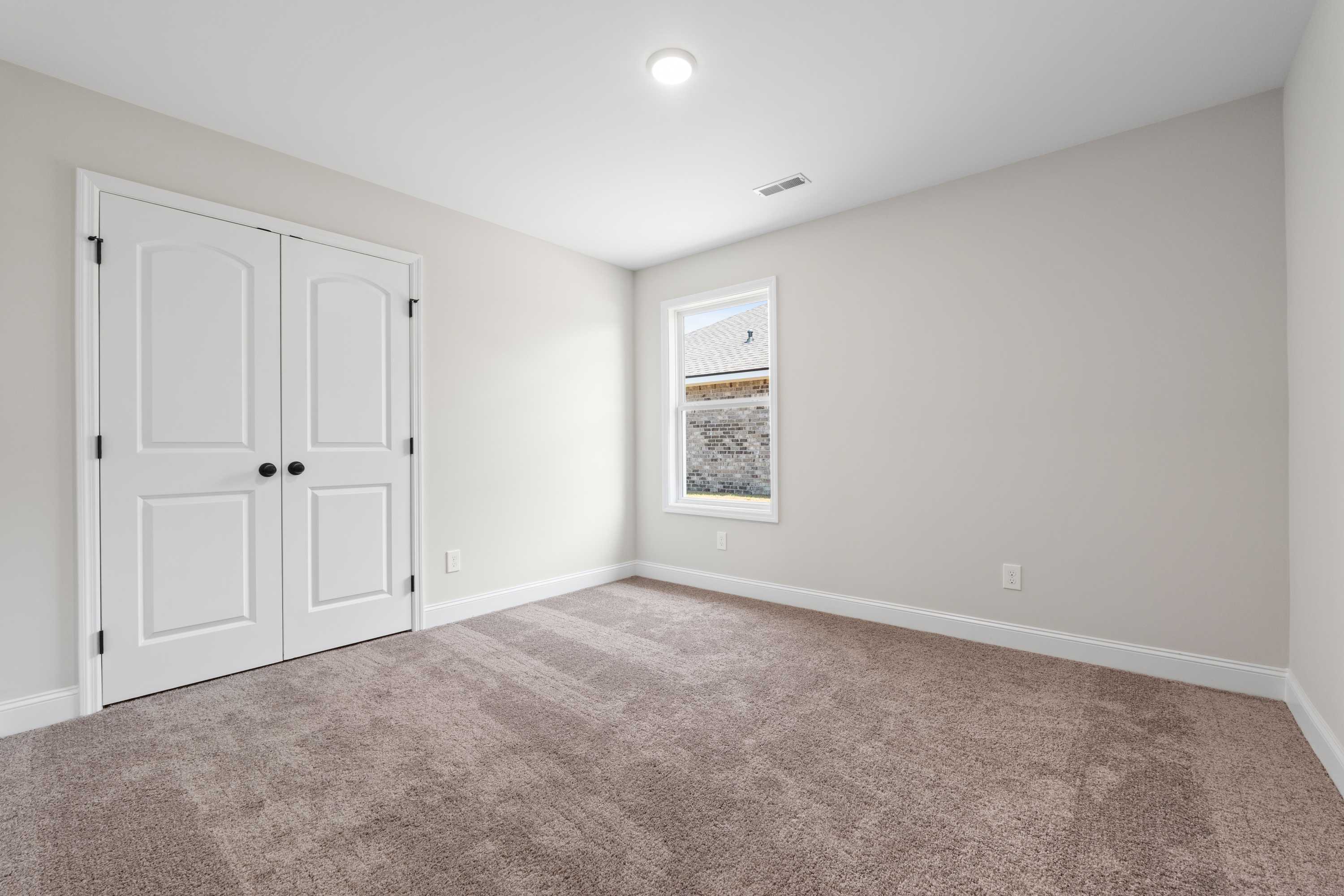 Spacious bedroom in The Everett C home with beige walls, white double closet doors, window view, and plush carpet flooring