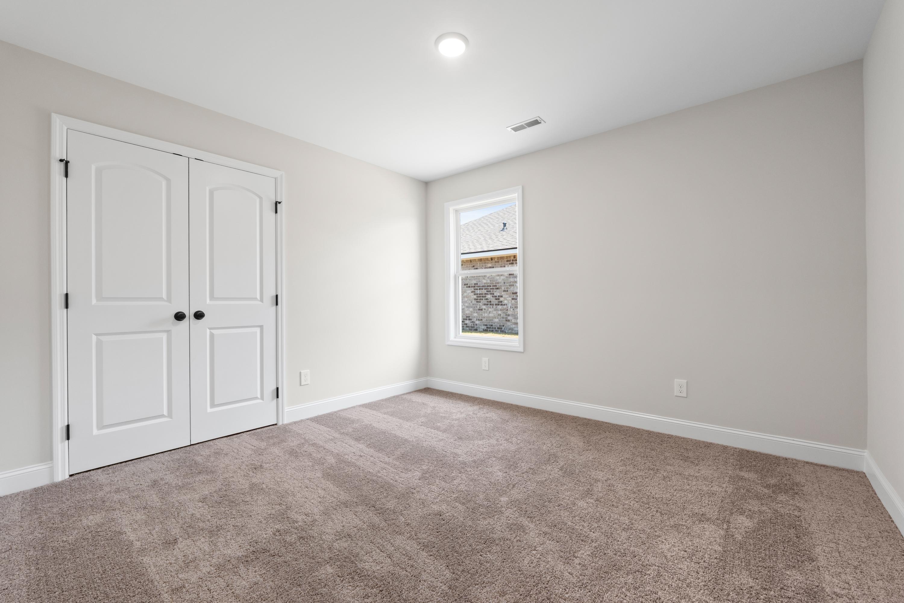 Spacious secondary bedroom in The Everett D with beige walls, white double closet doors, tan carpet, and large window