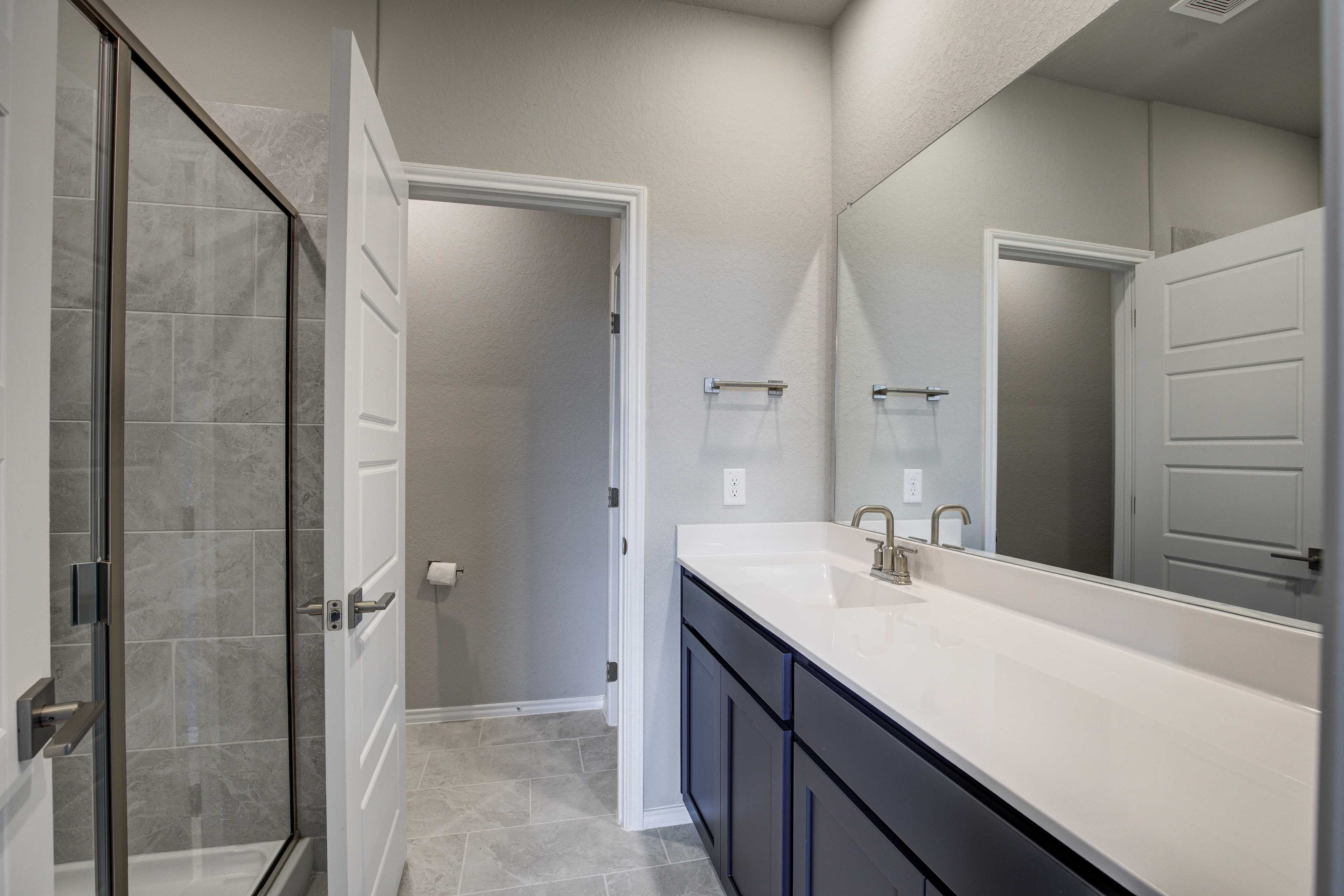 Spacious master bathroom in The Frio B with frameless glass shower, navy double vanity, subway tile, and neutral tones