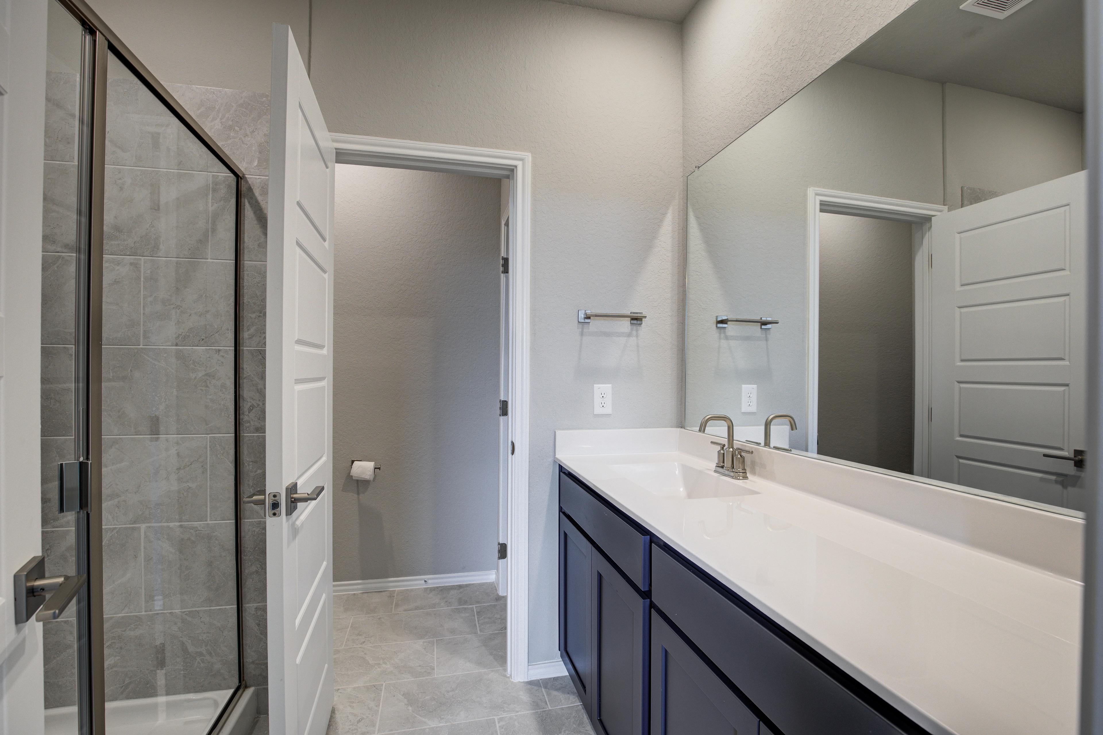 Spacious master bathroom in The Frio showcasing frameless glass shower, subway tile, double vanity with navy cabinets