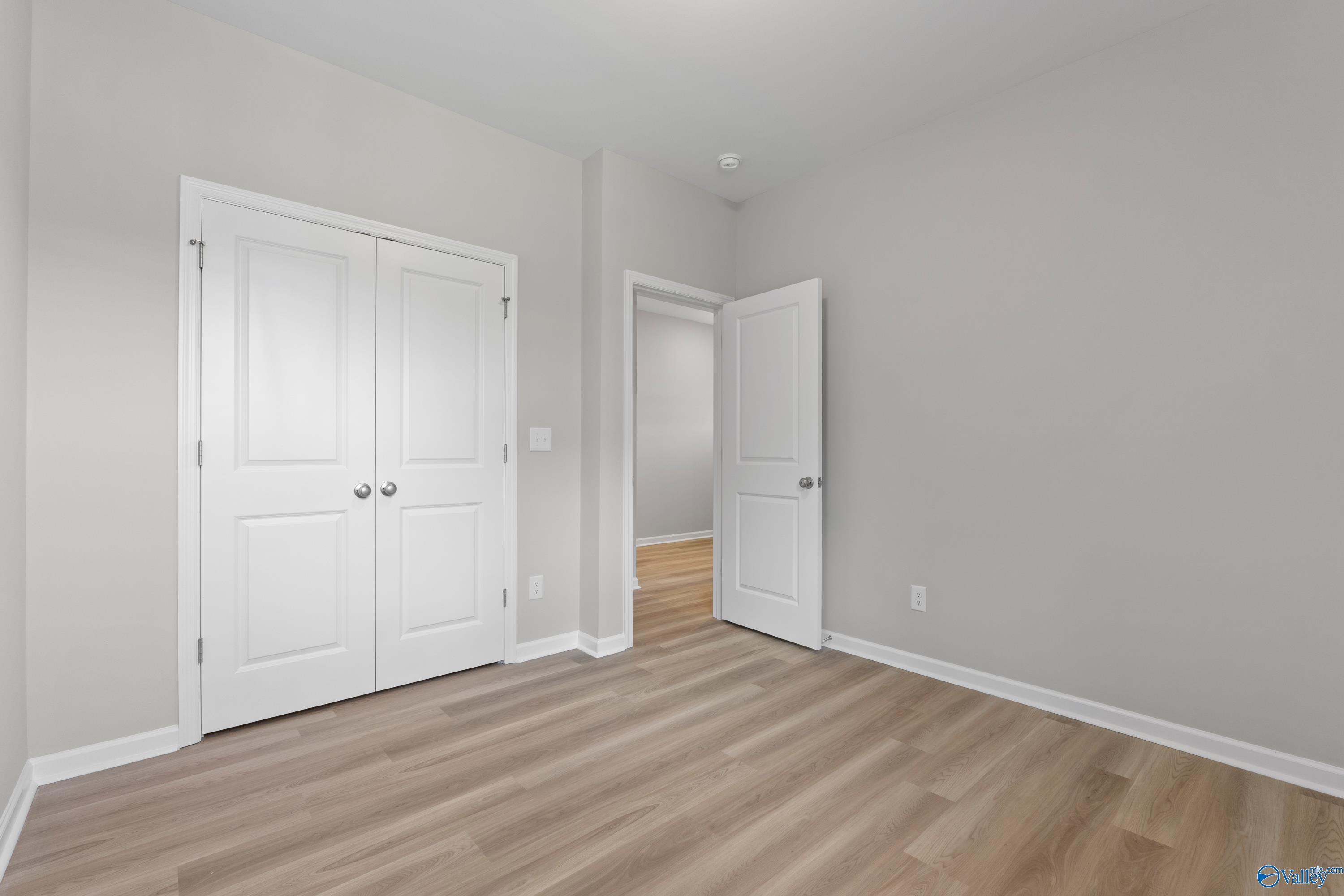 Bright secondary bedroom featuring double white closet doors, light gray walls, and hardwood-style floors in Davidson Homes The Polaris, Fayetteville, TN