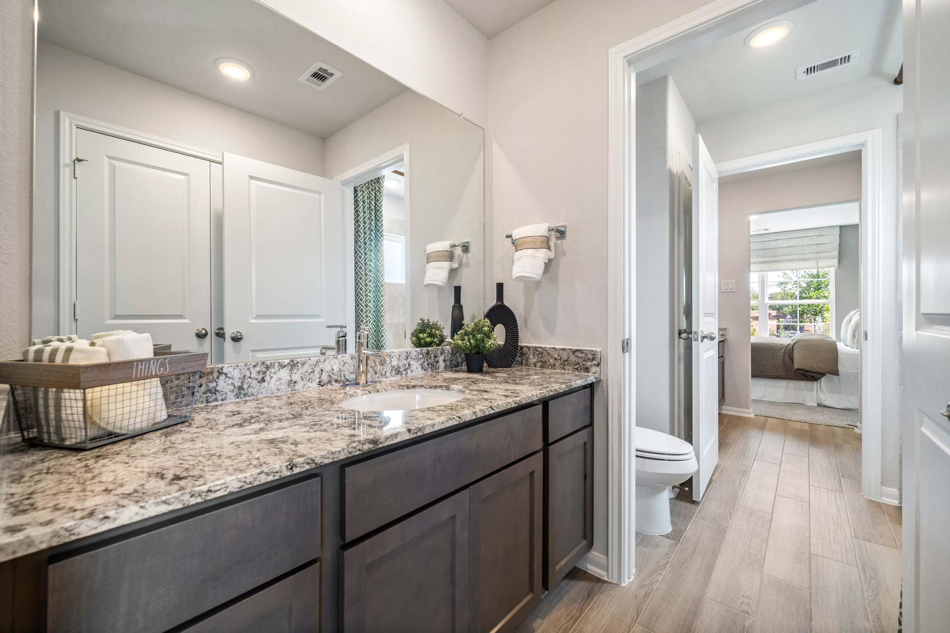 Spacious master bathroom at Windmill Estates in Magnolia Texas with double vanity, granite countertop, dark cabinets and wood floors
