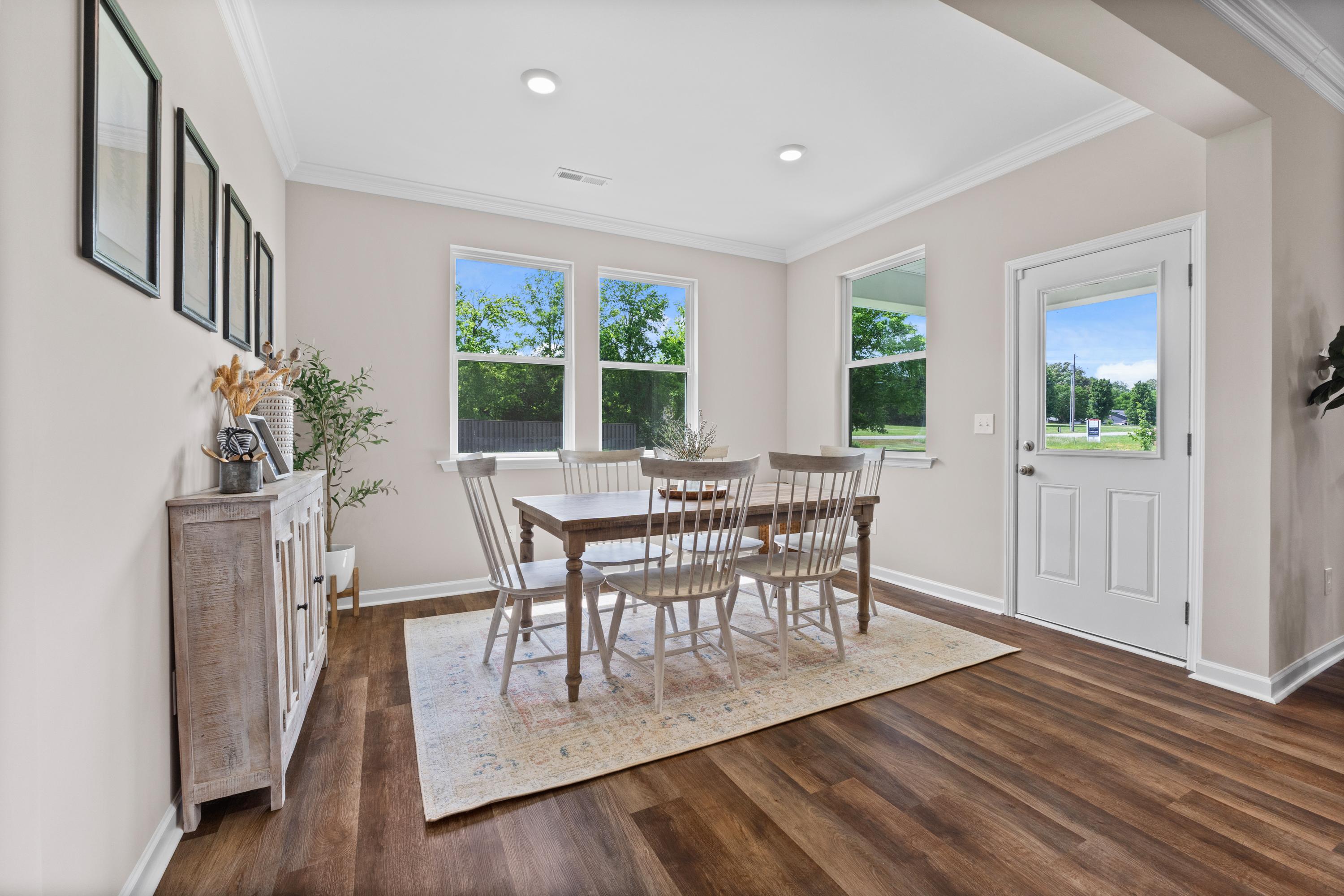 Bright dining room at Riverton Preserve in Huntsville Alabama with wooden table, white chairs, large windows, and hardwood floors