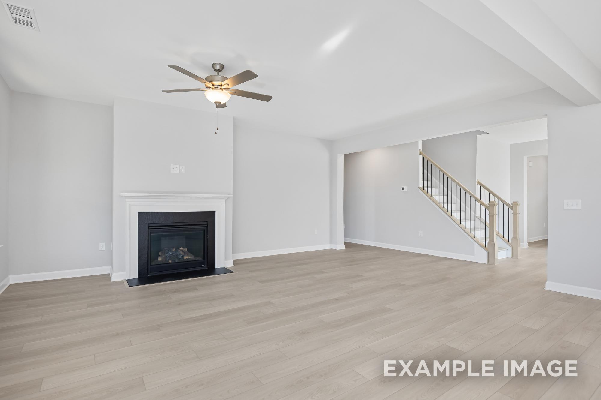 Spacious living room in The Cypress B II featuring gas fireplace, ceiling fan, hardwood floors, and open staircase
