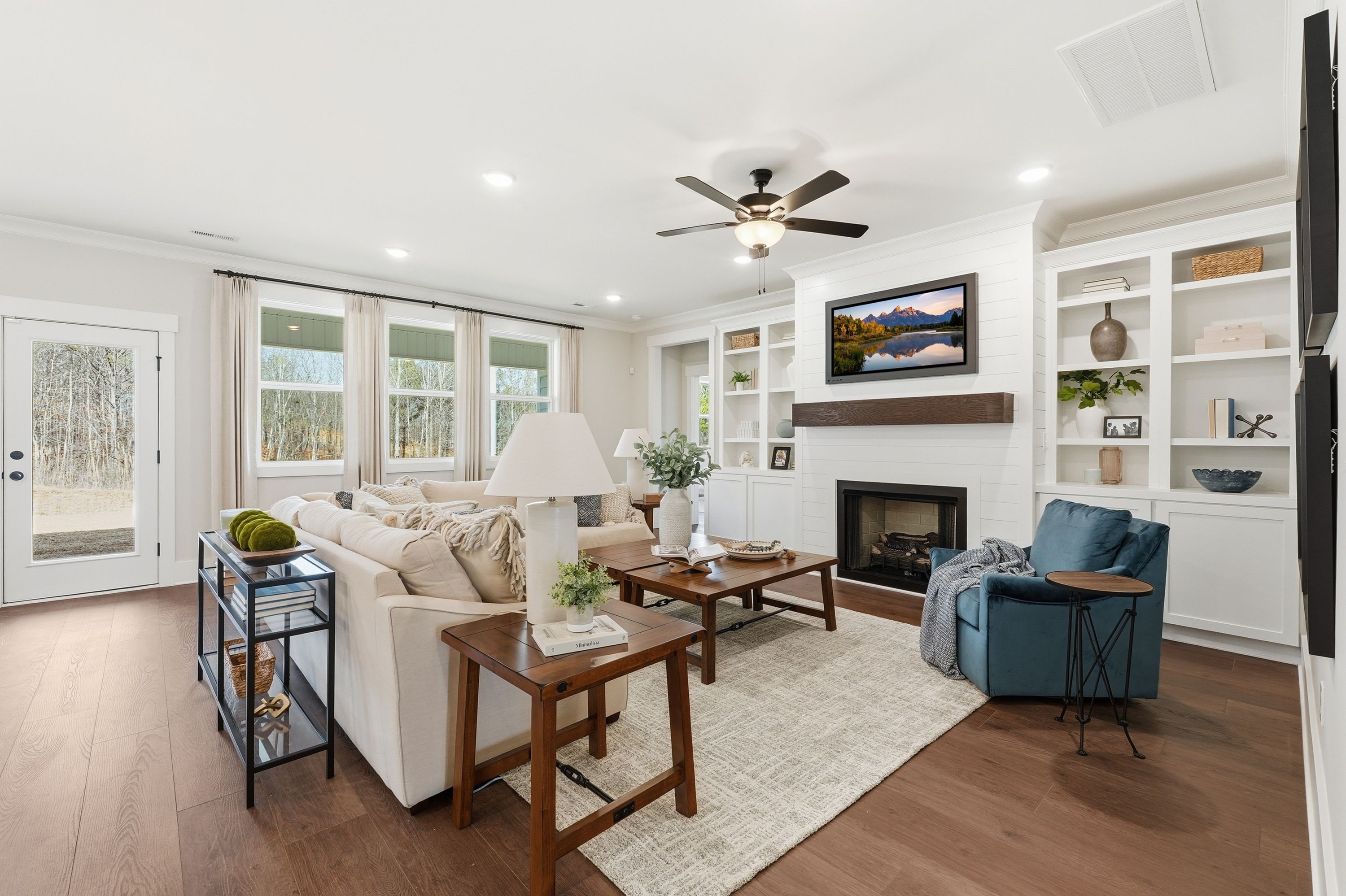Spacious living room in Noble Ridge Cullman AL with hardwood floors, beige sofa, gas fireplace, built-in shelves, and large windows