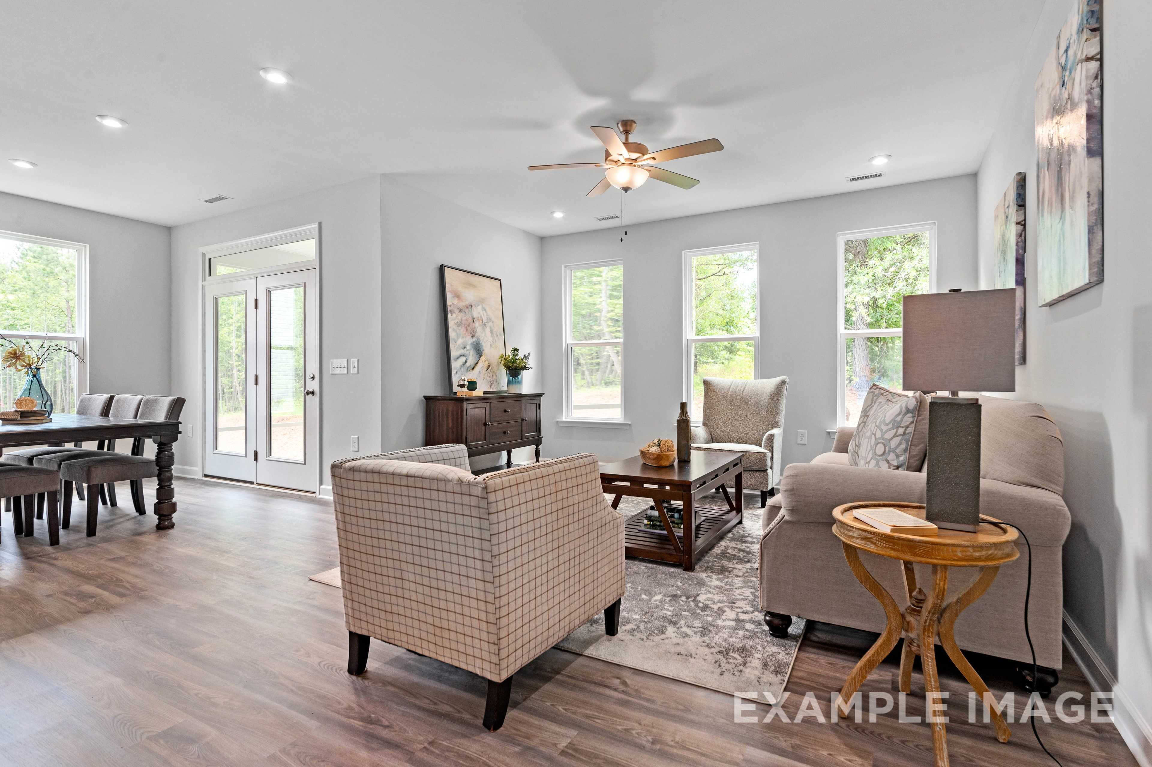 Open-concept living and dining in The Ash C home with hardwood floors, large windows, ceiling fan, beige sofa, and wooden table