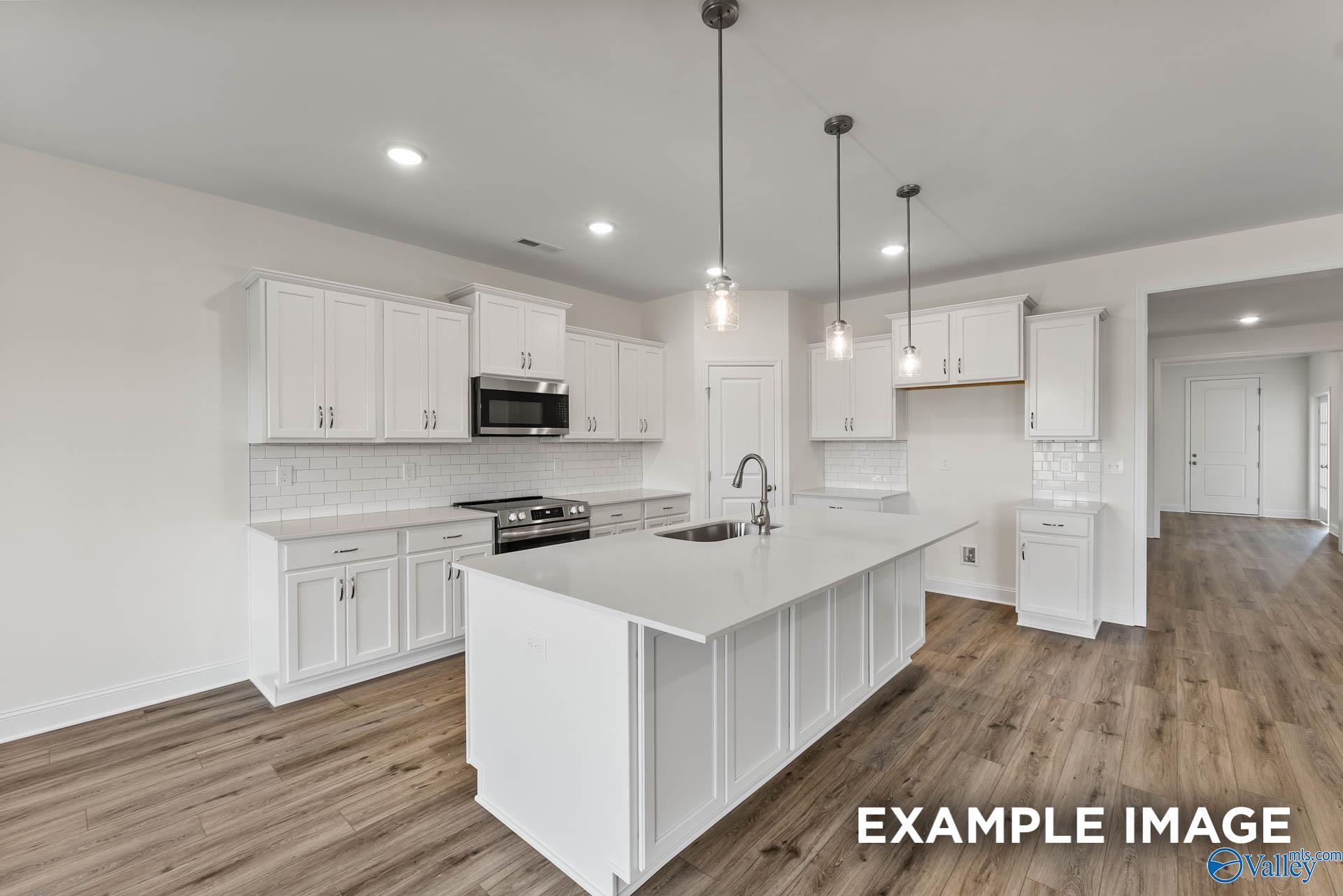 Modern kitchen with white cabinets, island, and wood-style flooring in The Harrison floor plan at Pikes Ridge, Meridianville.