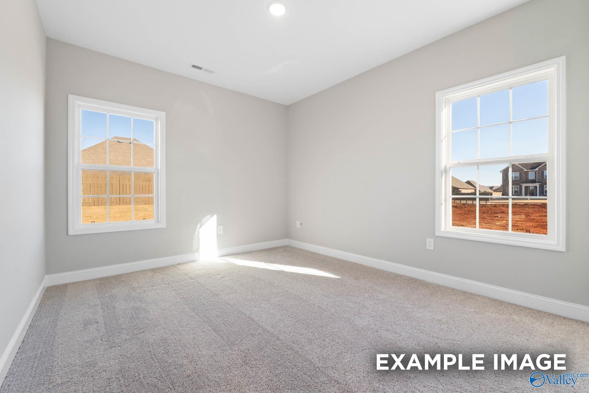 Spacious empty bedroom with gray walls, carpet floor, and large sunny windows in Davidson Homes The Valencia, Meridianville, Alabama