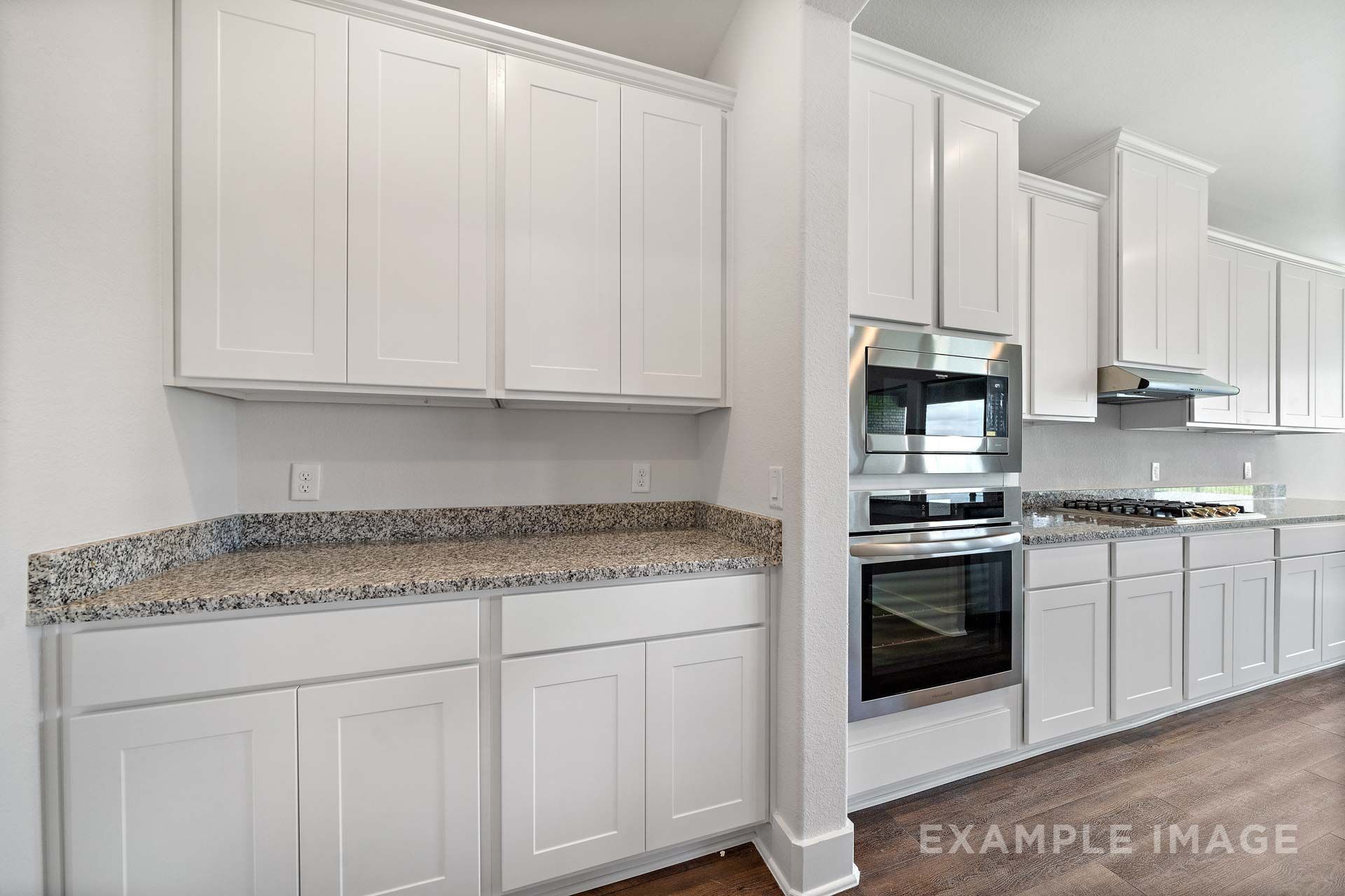 Modern kitchen in The Victoria by Davidson Homes featuring white shaker cabinets, granite countertops, and stainless steel appliances.