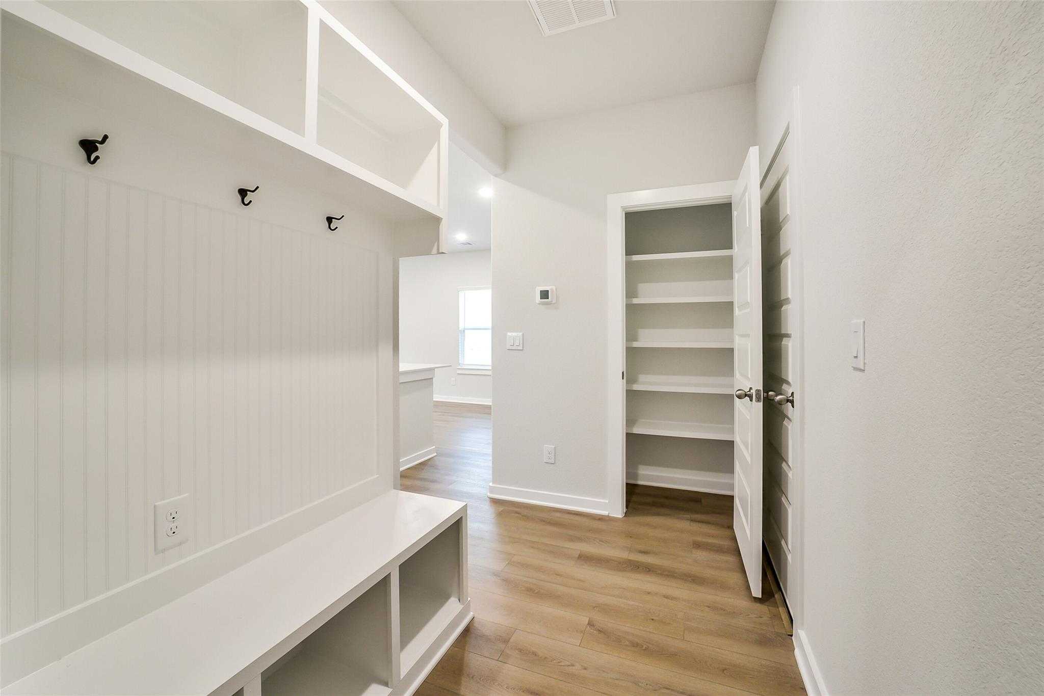 White mudroom with built-in lockers, coat hooks, bench, and pantry closet in Davidson Homes The Blanco E, Magnolia Texas