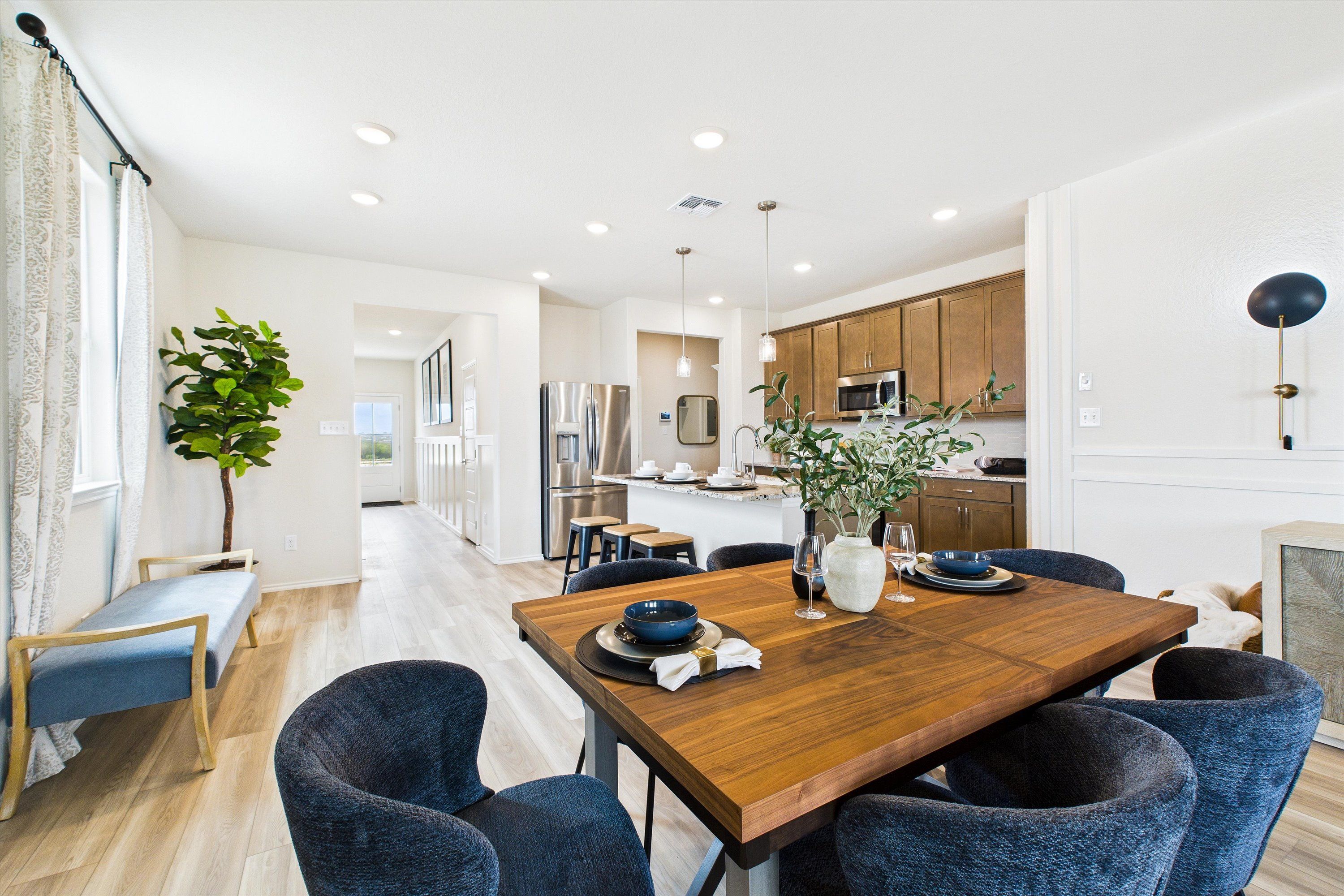 Spacious open-concept kitchen and dining area in Agave San Antonio TX home with wooden table, blue velvet chairs, oak cabinets