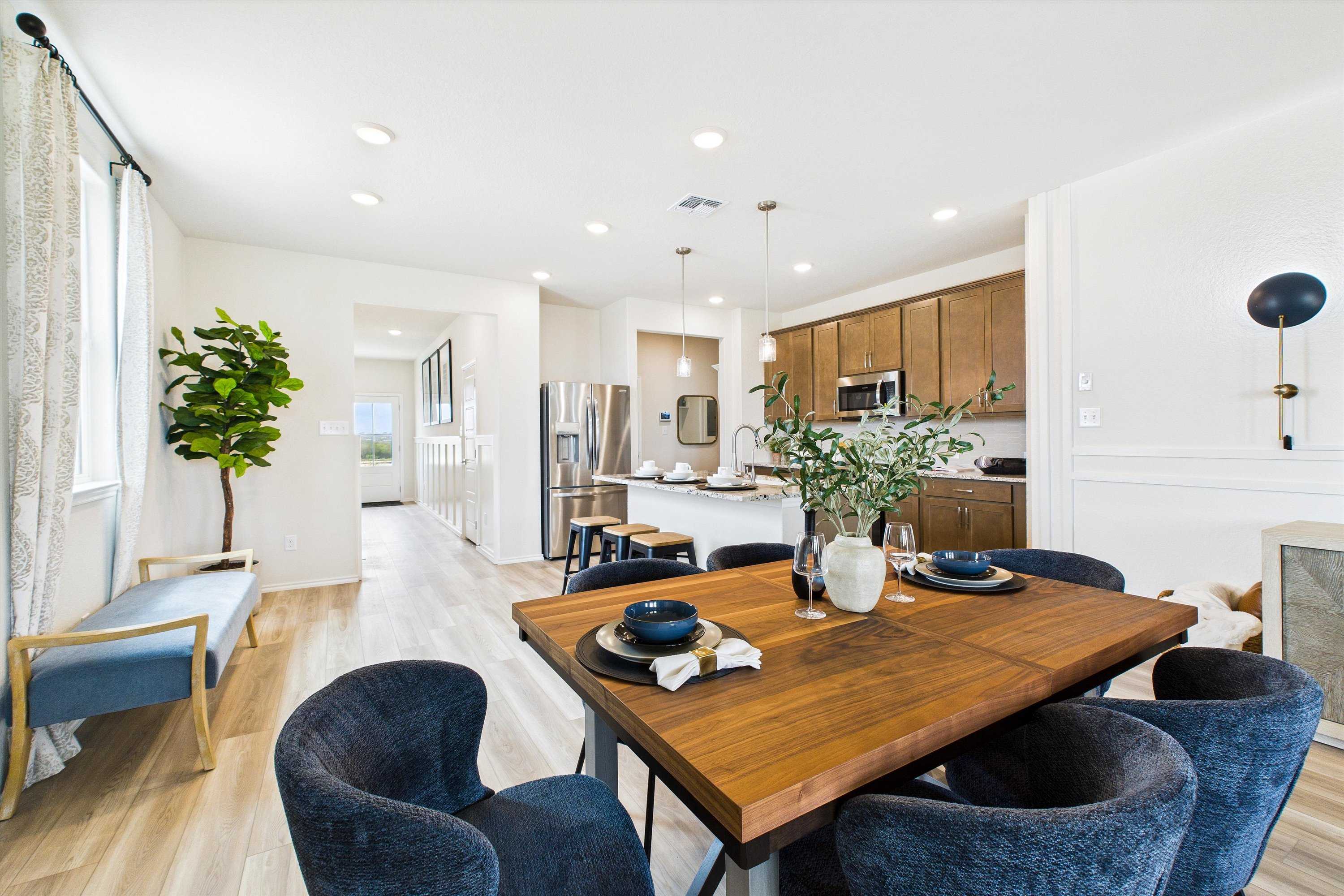 Spacious open-concept kitchen and dining area in Agave San Antonio TX home with wooden table, blue velvet chairs, oak cabinets