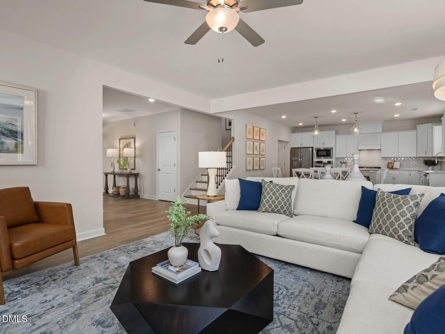 Inviting living room with white sectional sofa, leather armchair, and open kitchen in 5-bedroom Davidson Homes The Hickory II D, Wake Forest, NC