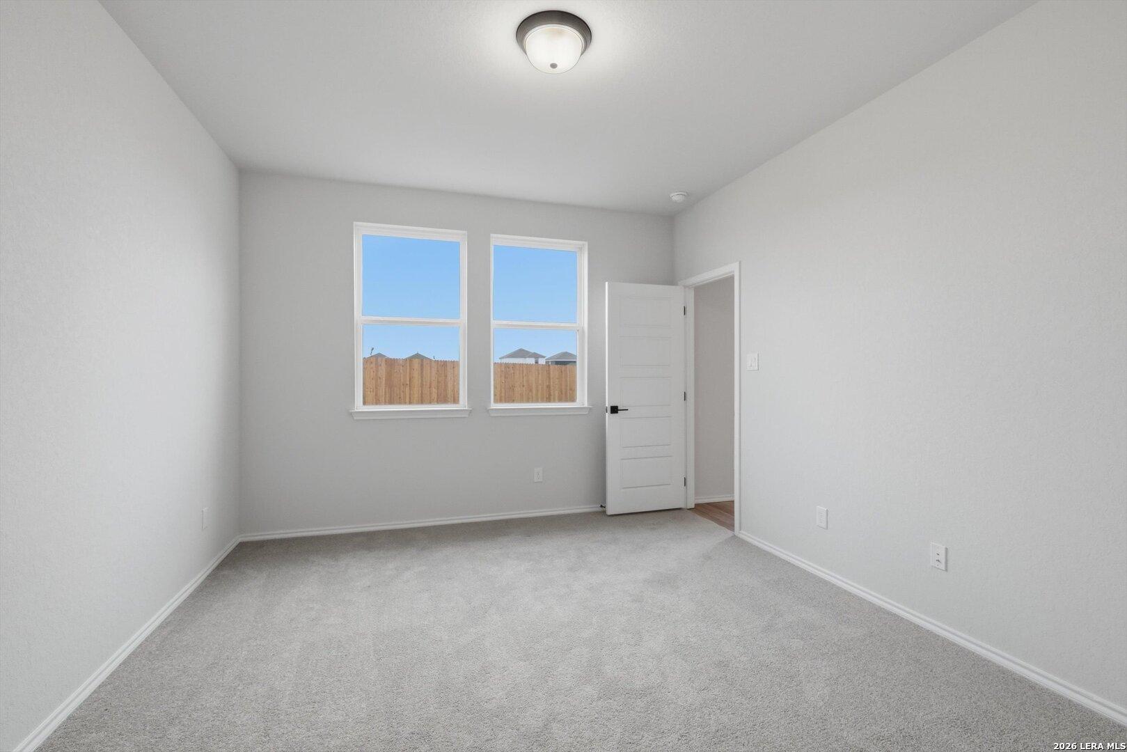 Bright bedroom with gray walls and carpet, large windows showing fenced backyard, open door in Davidson Homes The Blanco C, San Antonio