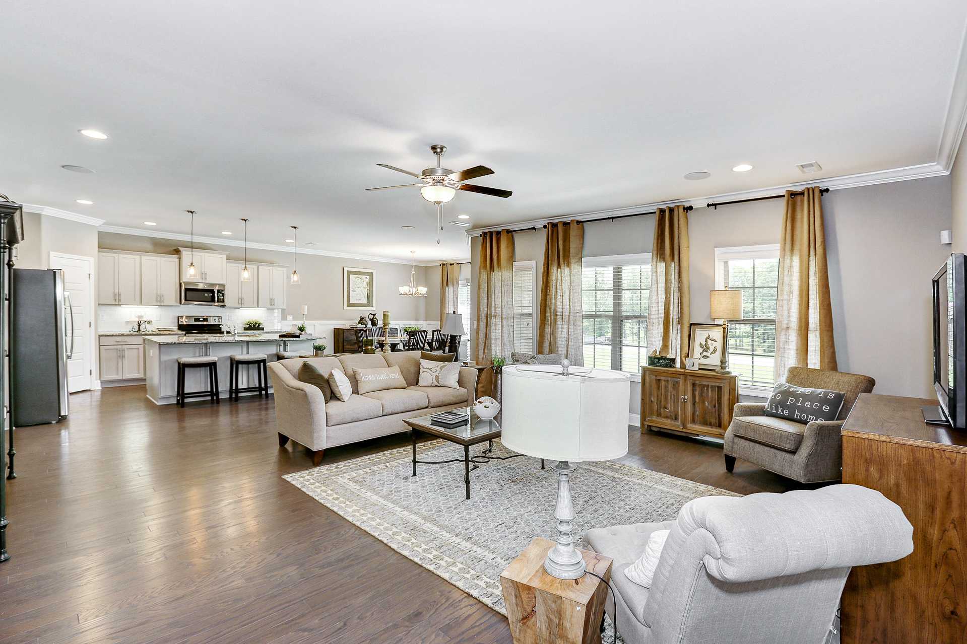 Open-concept living room and kitchen in Stone Creek Phase II Cullman Alabama with hardwood floors, beige sofa, and large windows